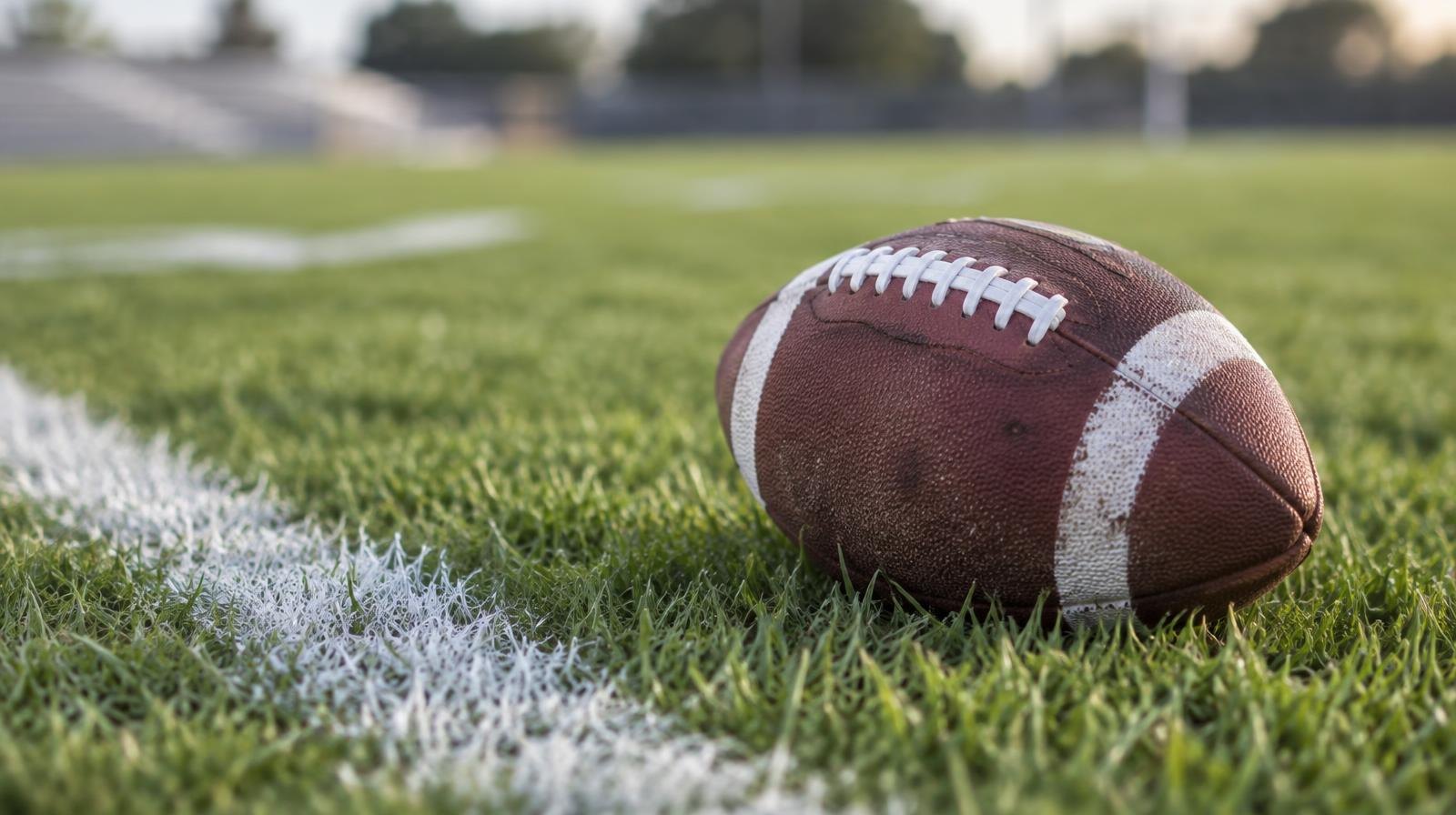 An American football resting on green grass near a white yard line.