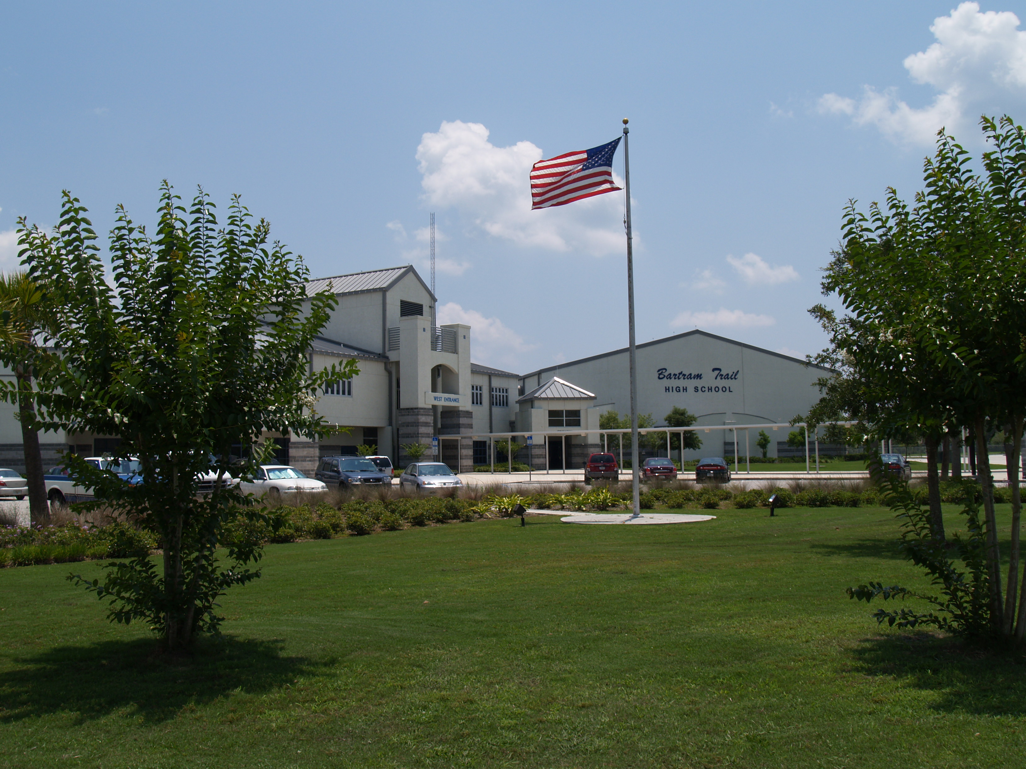Exterior of a high school building with a flagpole and parking lot in front.