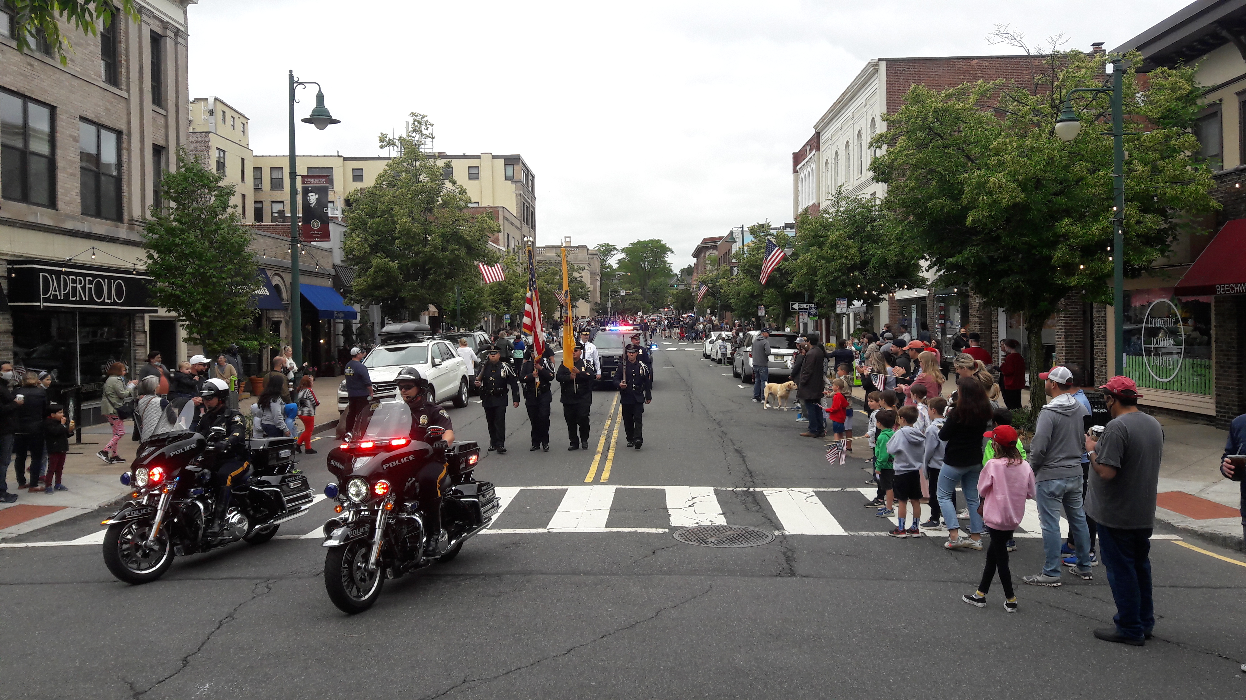 Families lining a downtown street in Summit, New Jersey with storefronts visible.