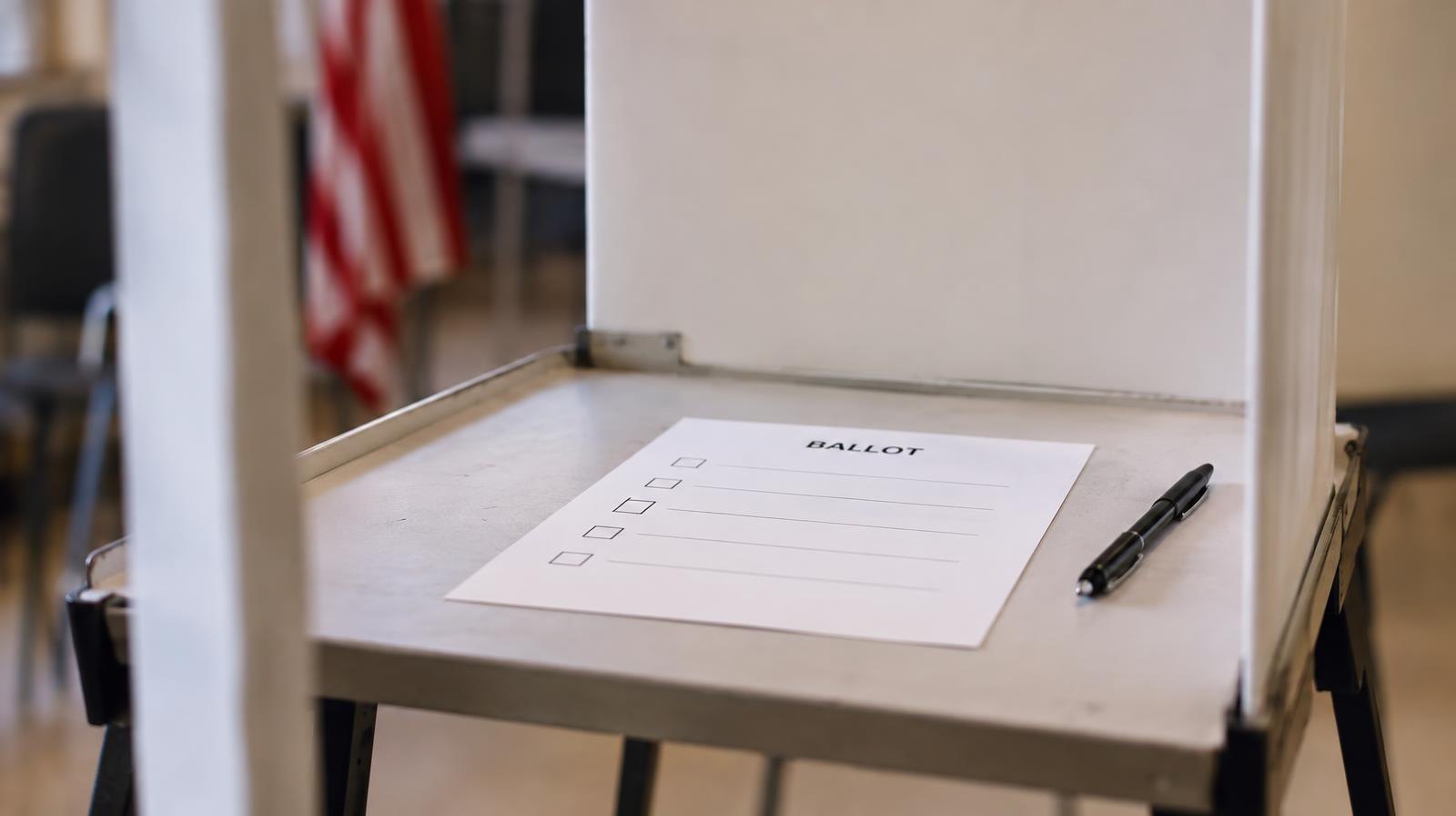 A blank paper ballot resting in a voting booth with a black pen beside it.