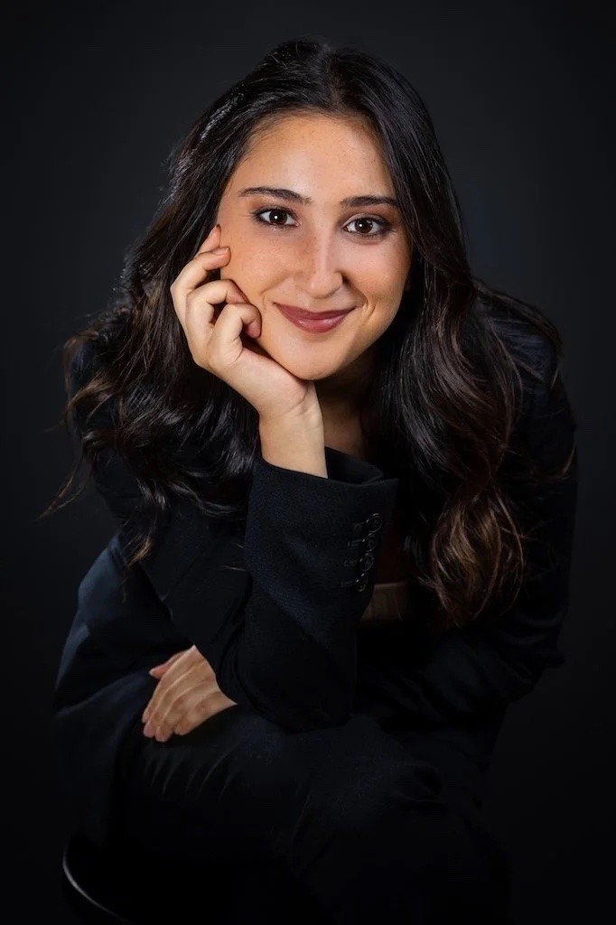 A smiling woman in a black blazer poses for a professional portrait.