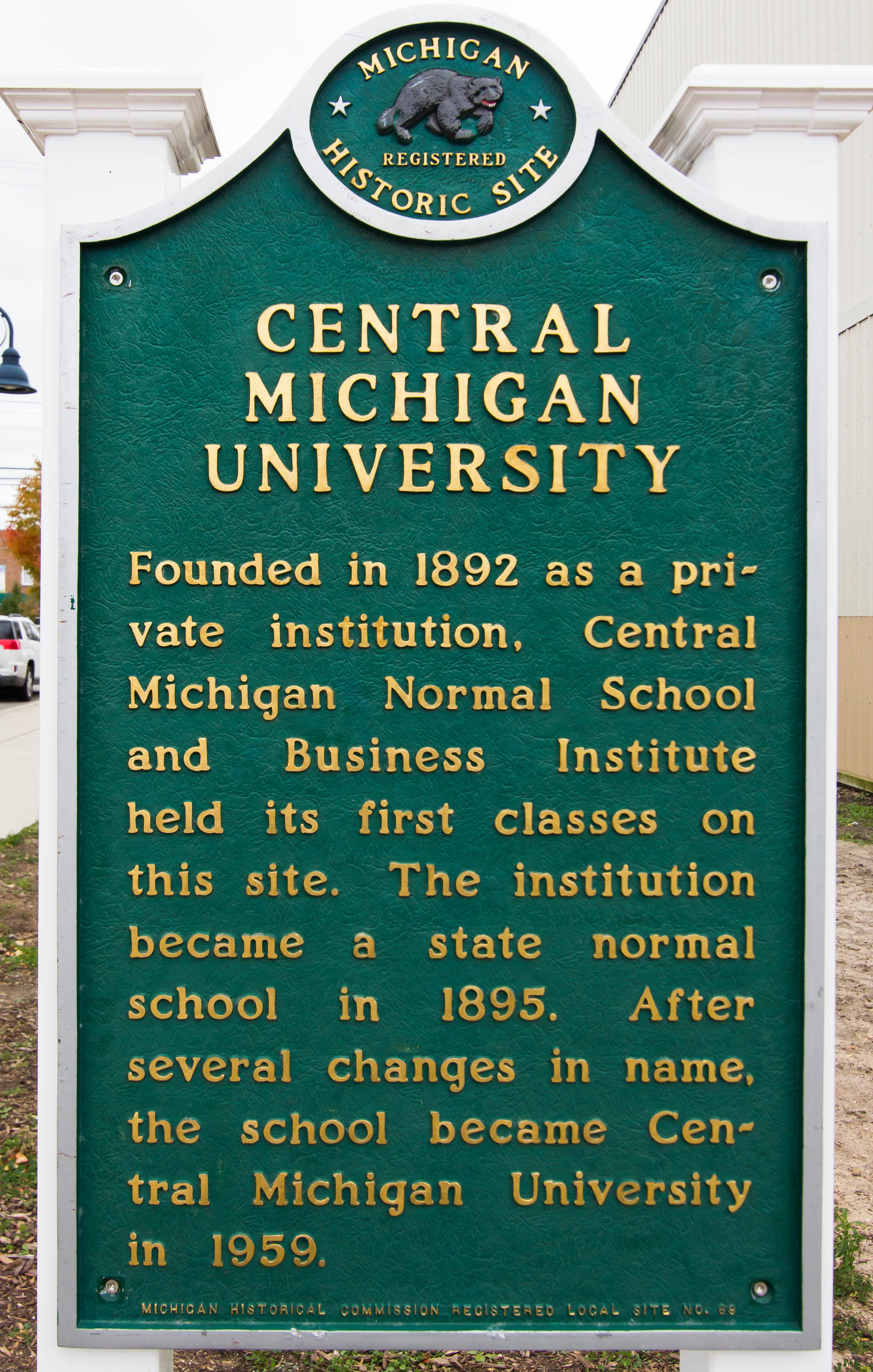 Green historic site marker for Central Michigan University between white columns.