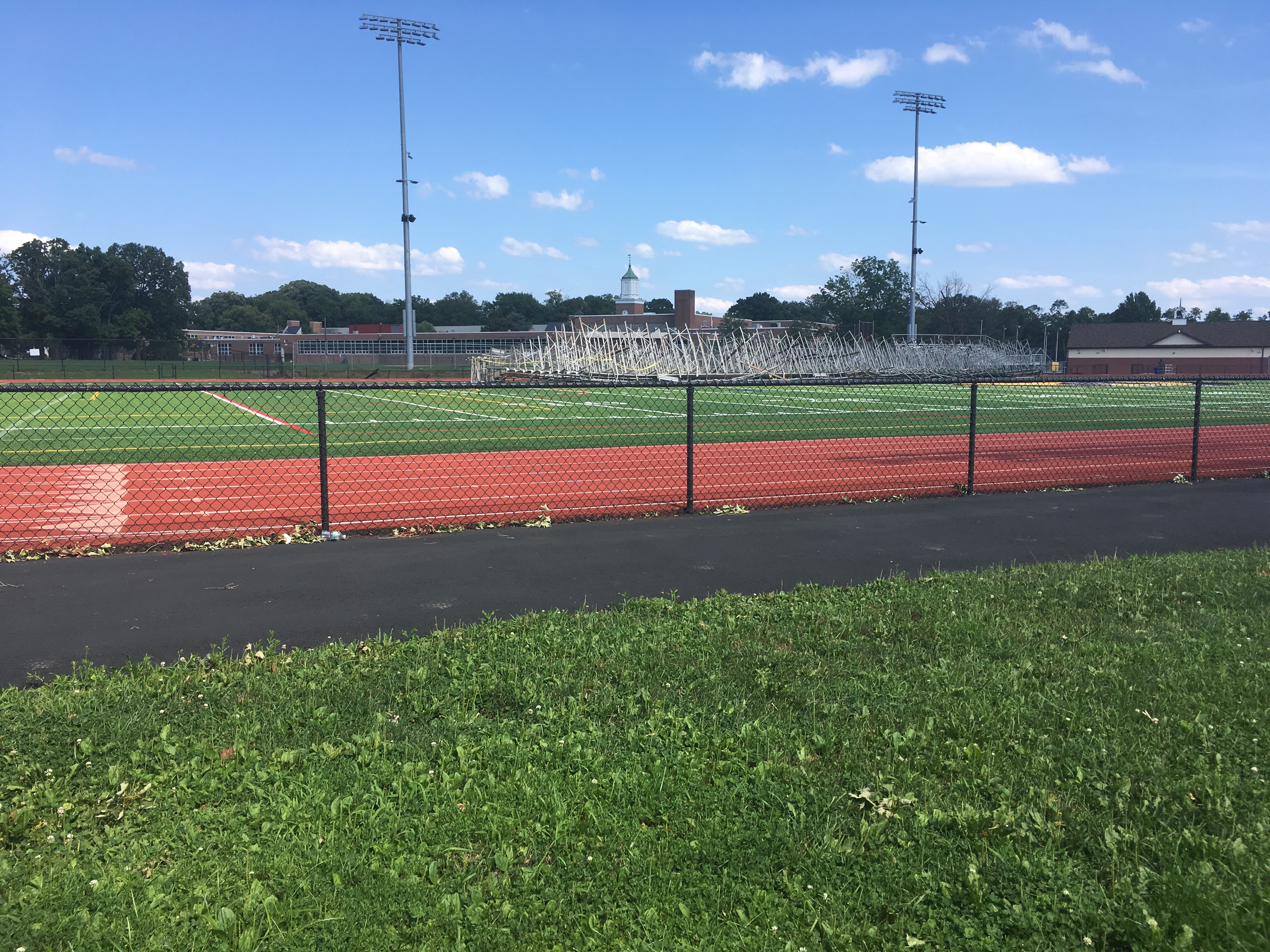Red running track and football field with metal bleachers at a high school campus.