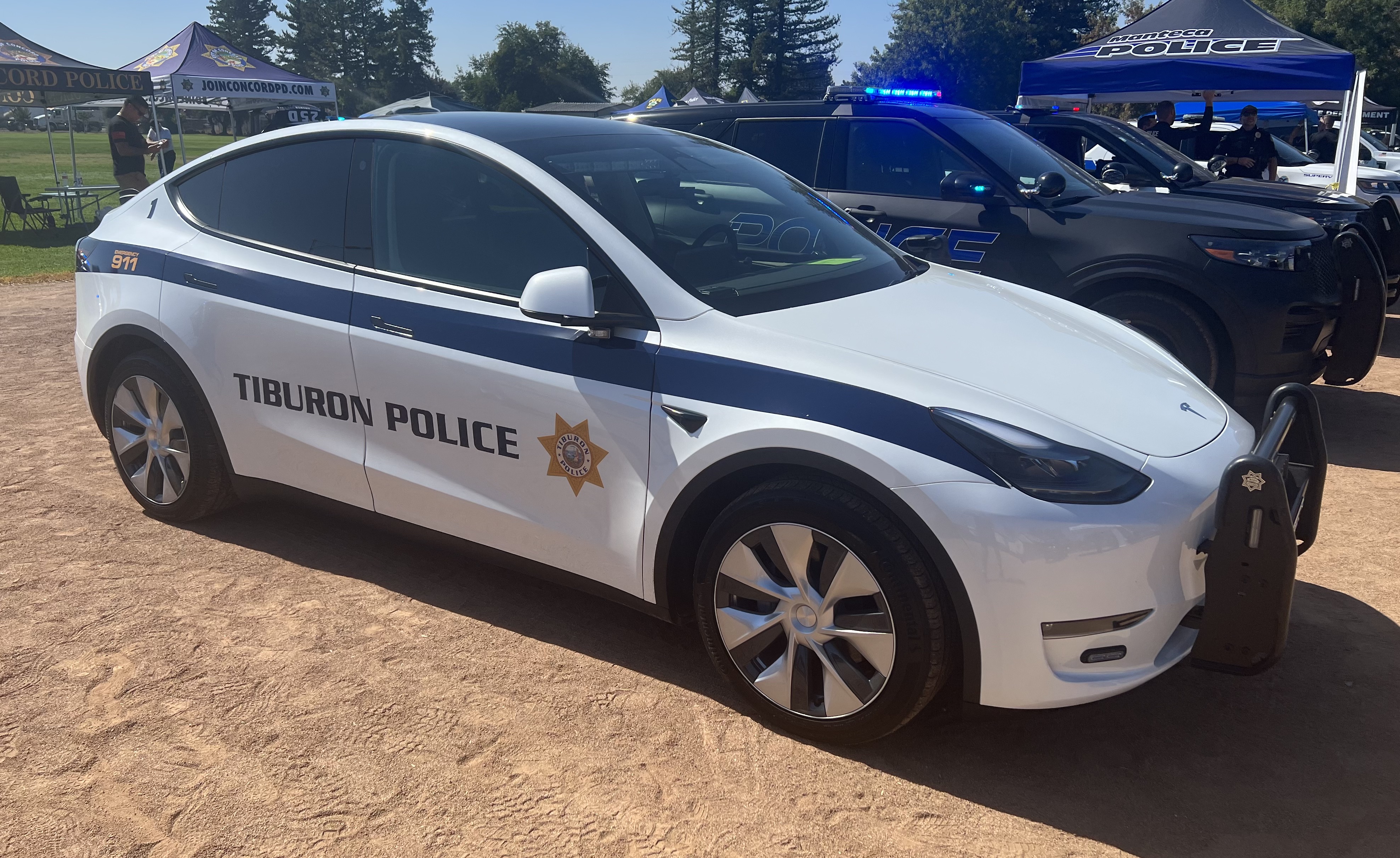 White Tesla Model Y patrol car with Tiburon Police Department markings on the door.