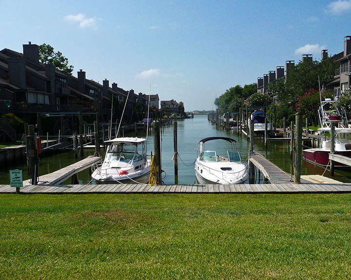 Two white motorboats docked at wooden piers along a narrow residential canal.
