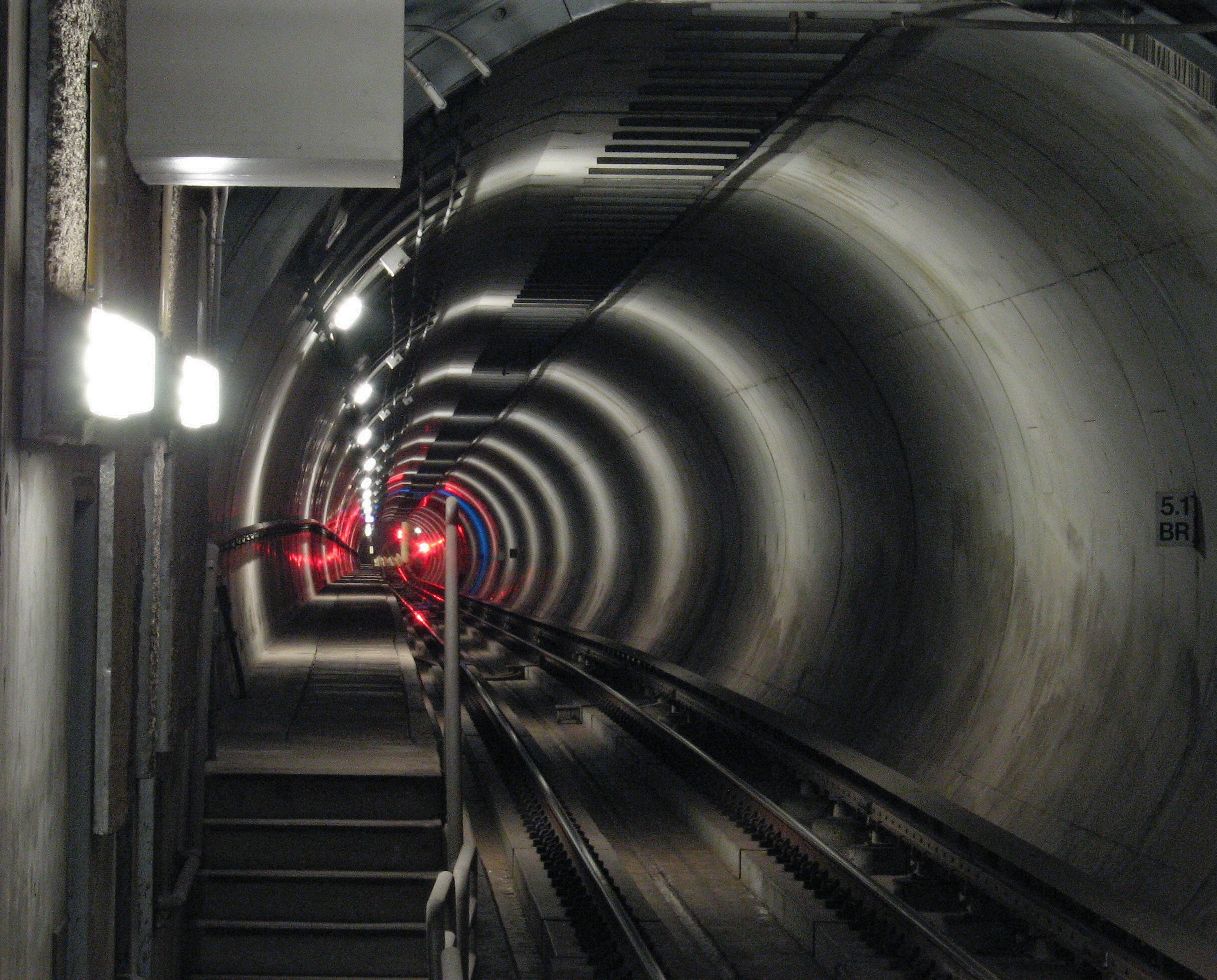 Circular subway tunnel with rail tracks and red and blue signal lights in the distance.