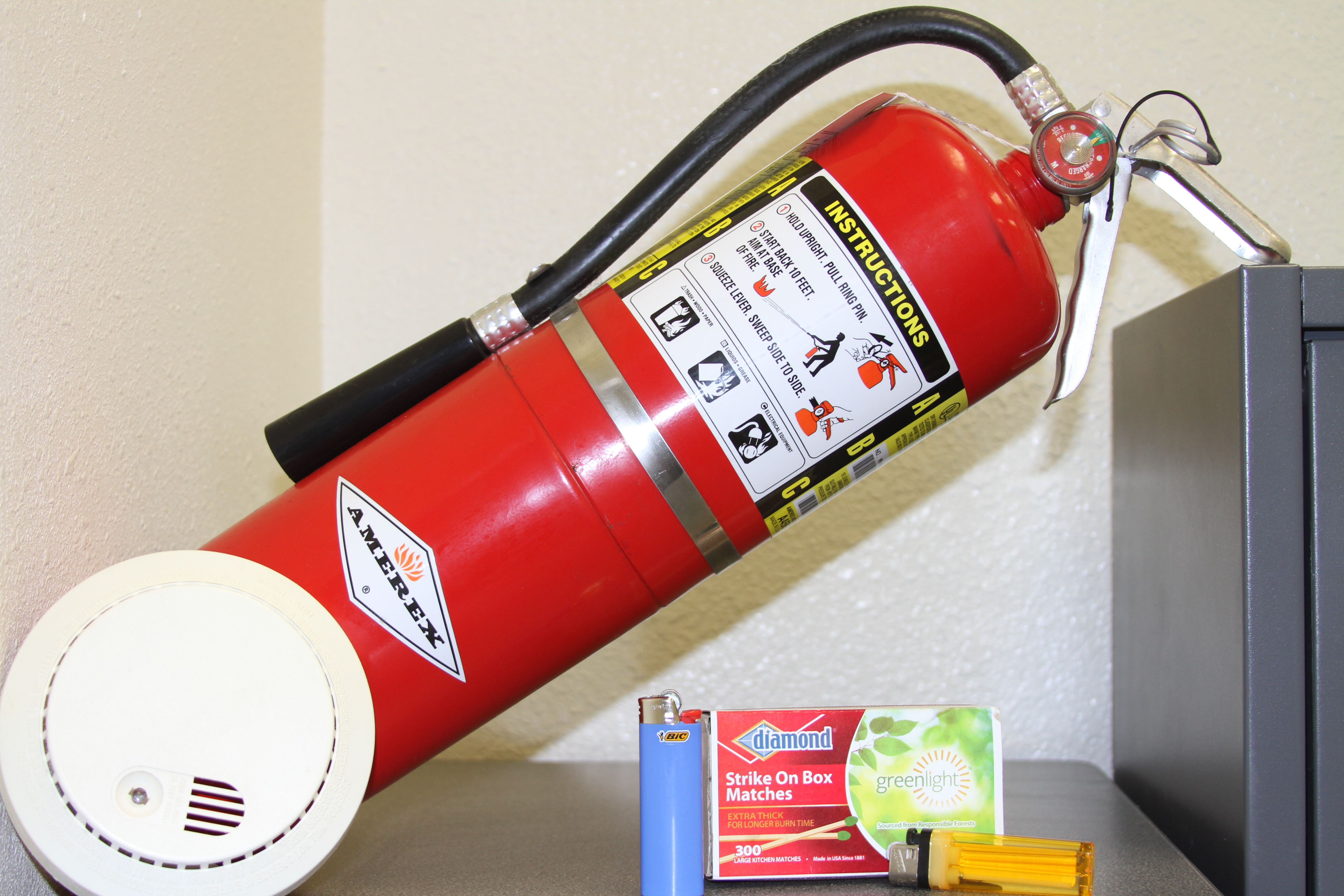 A red fire extinguisher, white smoke detector, lighter, and matchbox on a surface.