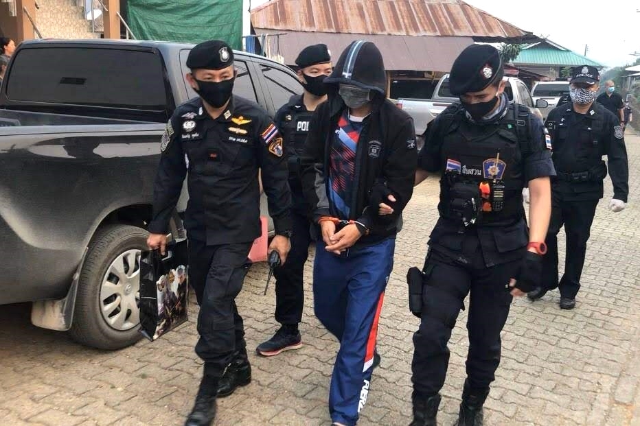 Masked officers in black uniforms escorting a handcuffed suspect outdoors near a vehicle.