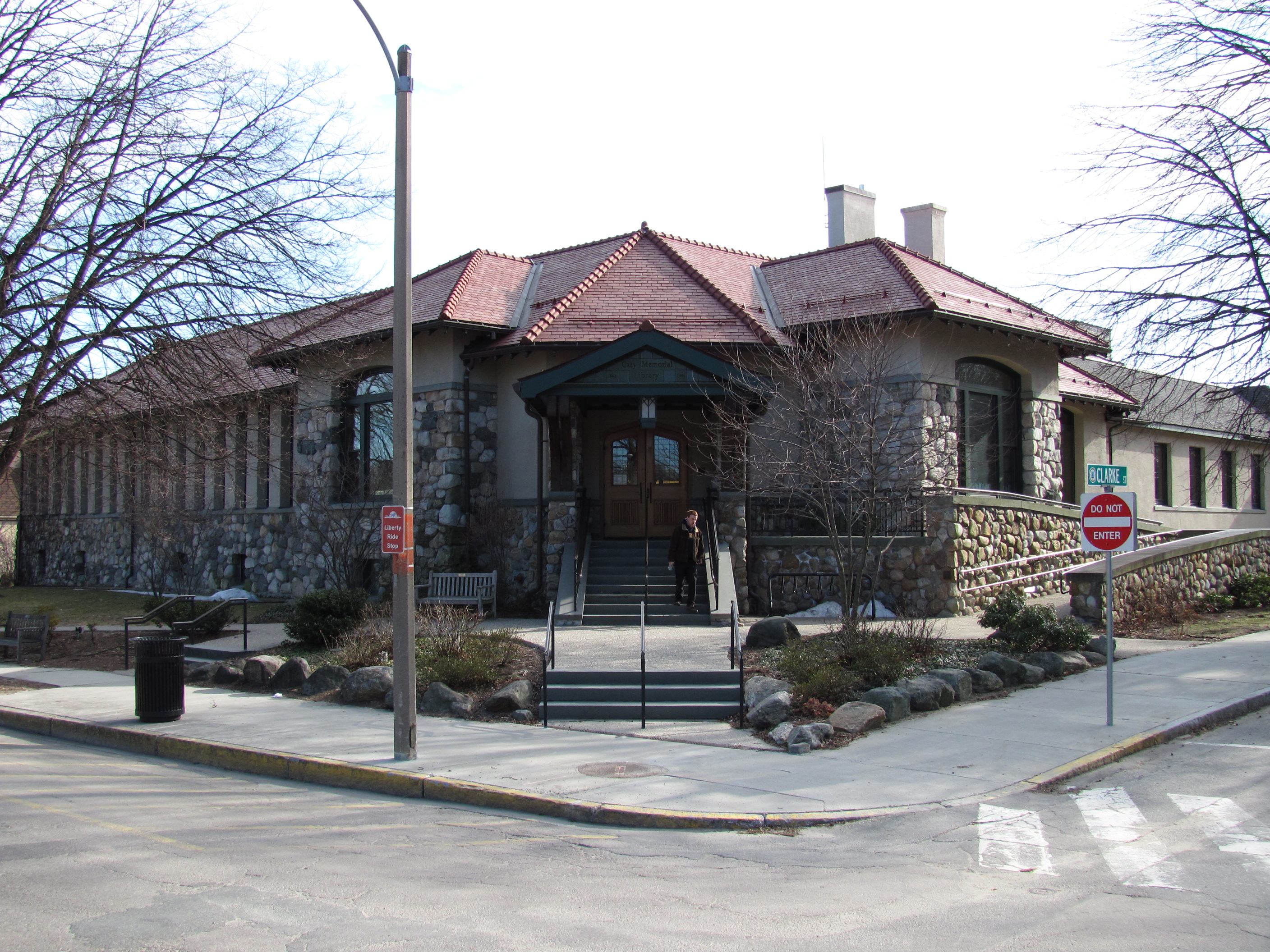 Stone library building with a red tile roof at a street corner, bare trees in winter.