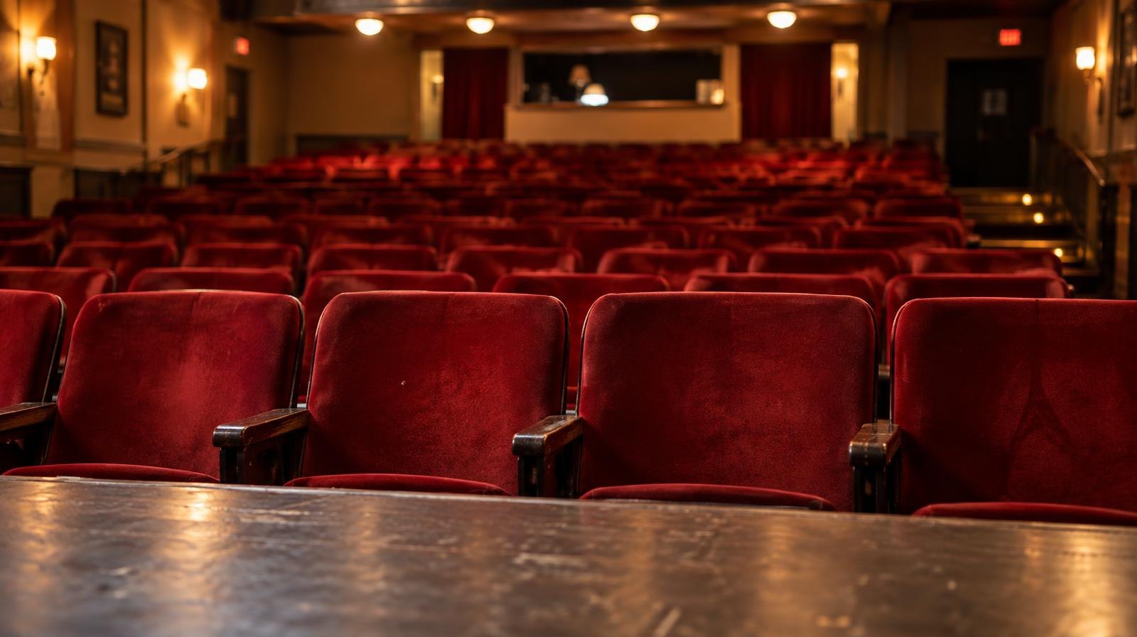 Rows of empty red velvet seats in a small theater auditorium.