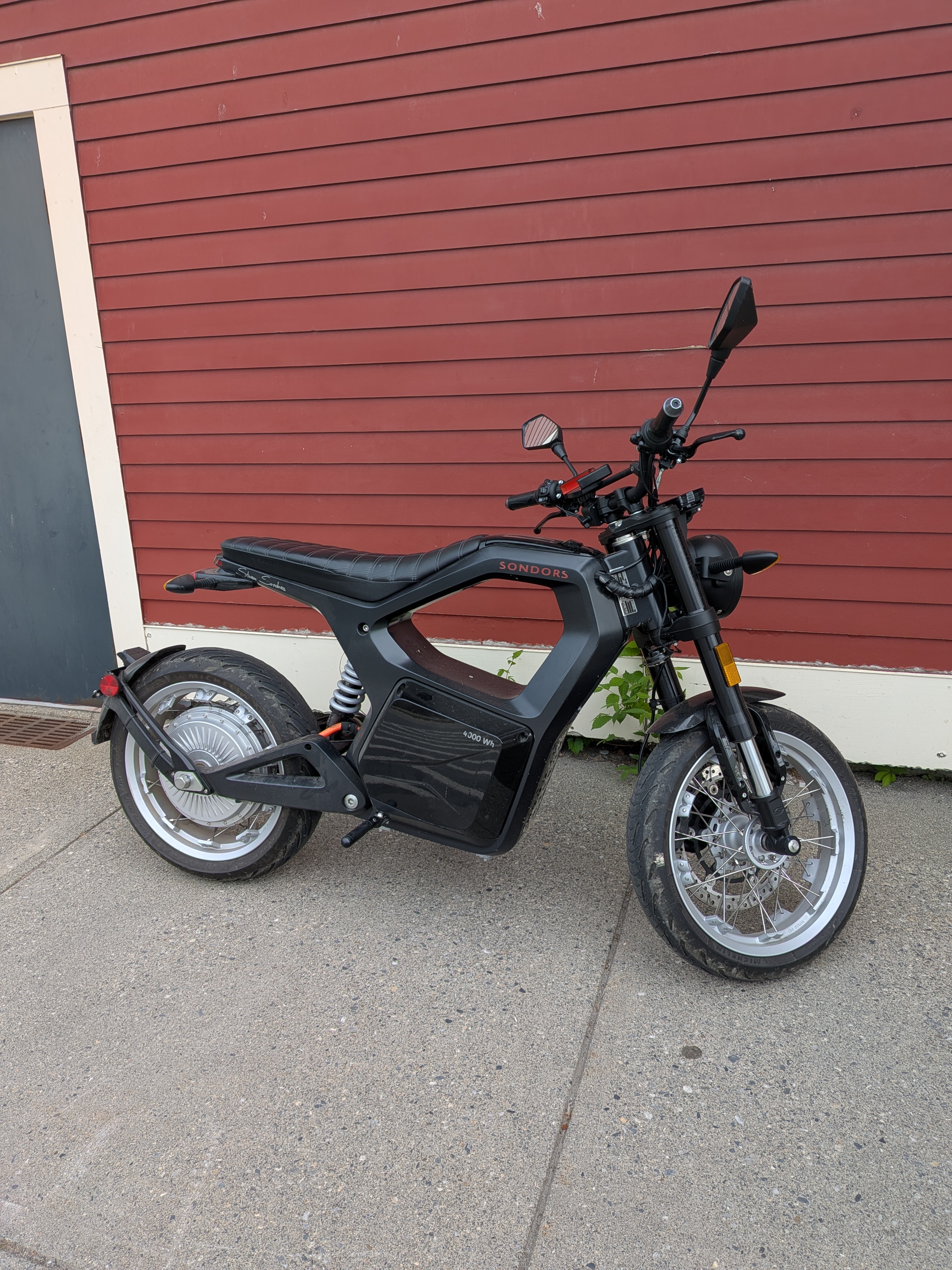 Electric motorcycle parked on a sidewalk in front of a store building.