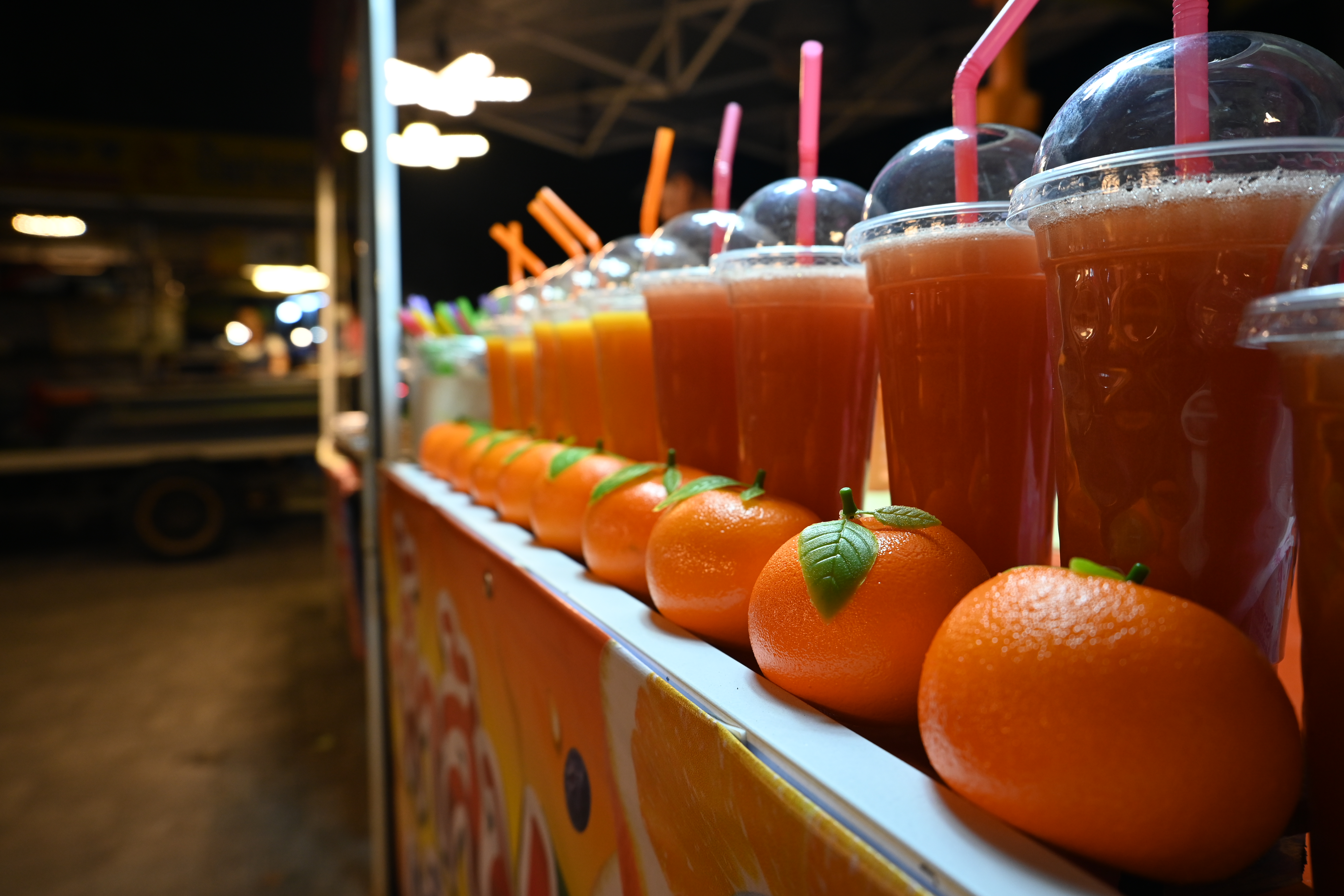 Rows of colorful fresh fruit juice cups with domed lids and straws on a counter.