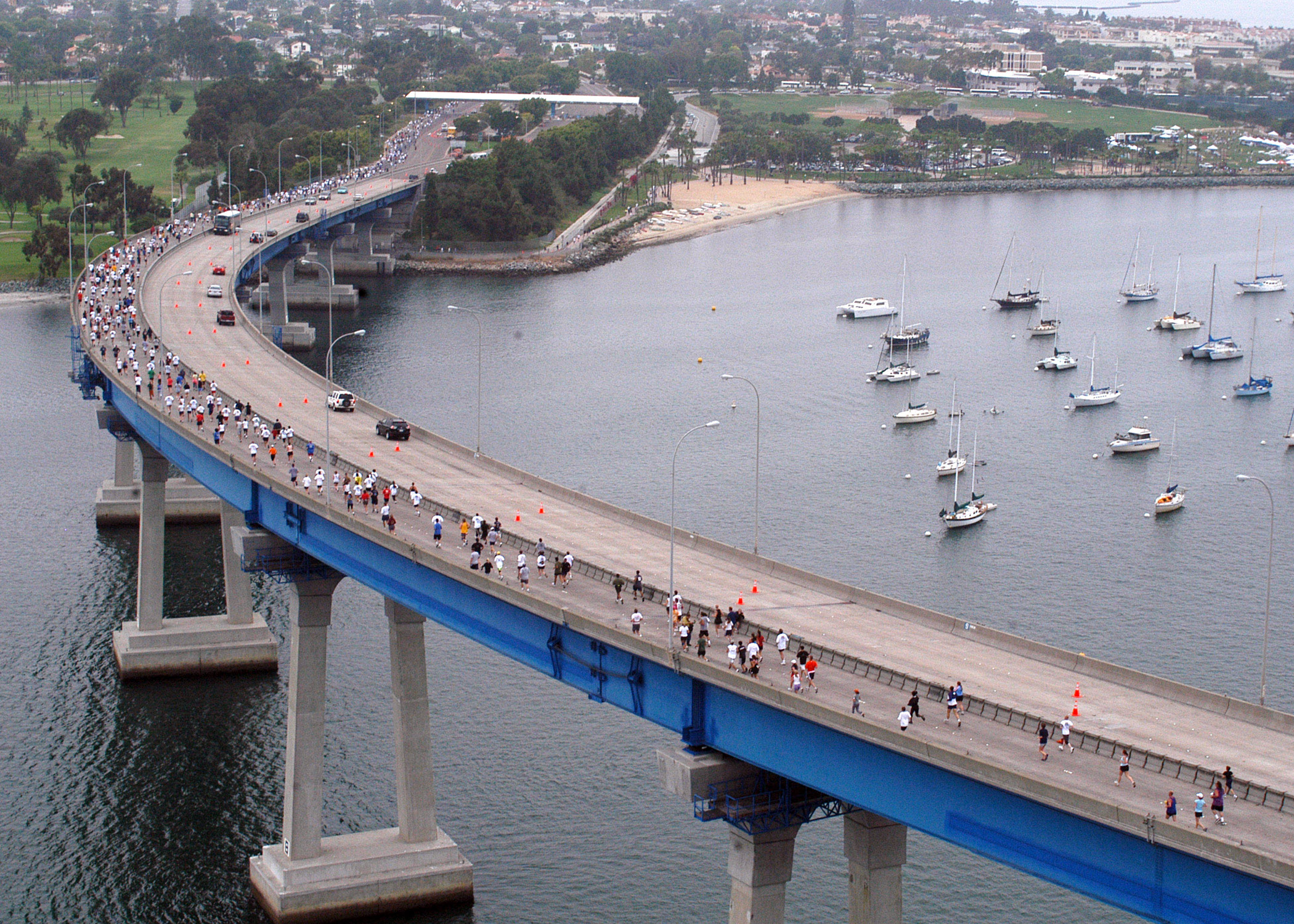 Aerial view of a curved bridge over a bay with a park and waterfront visible below.