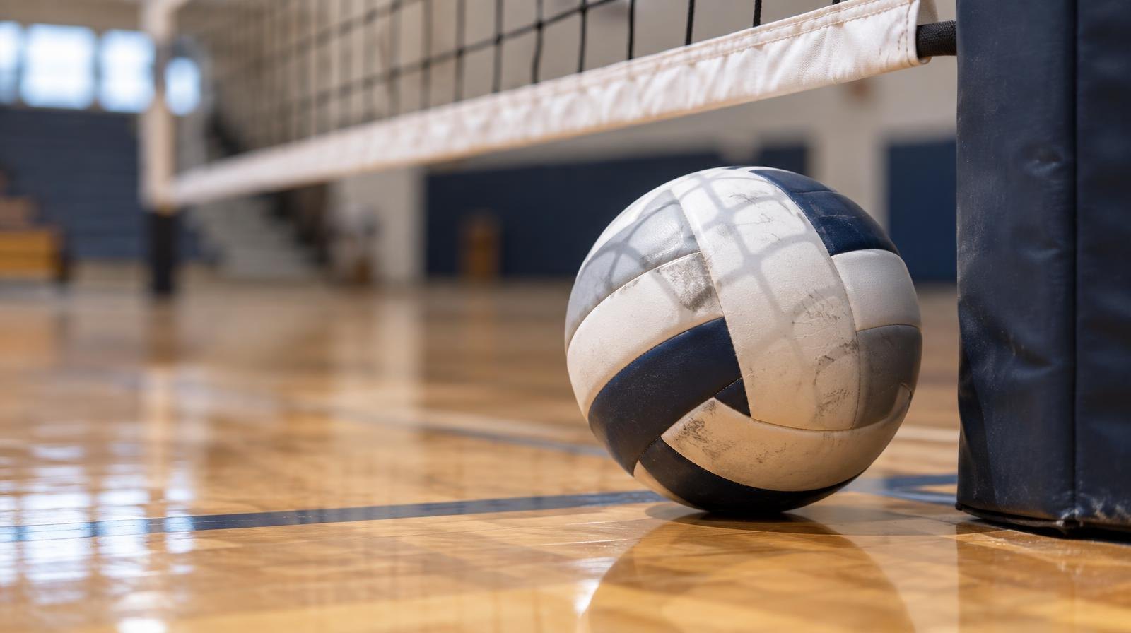 A volleyball resting on a gym floor beside a net post.
