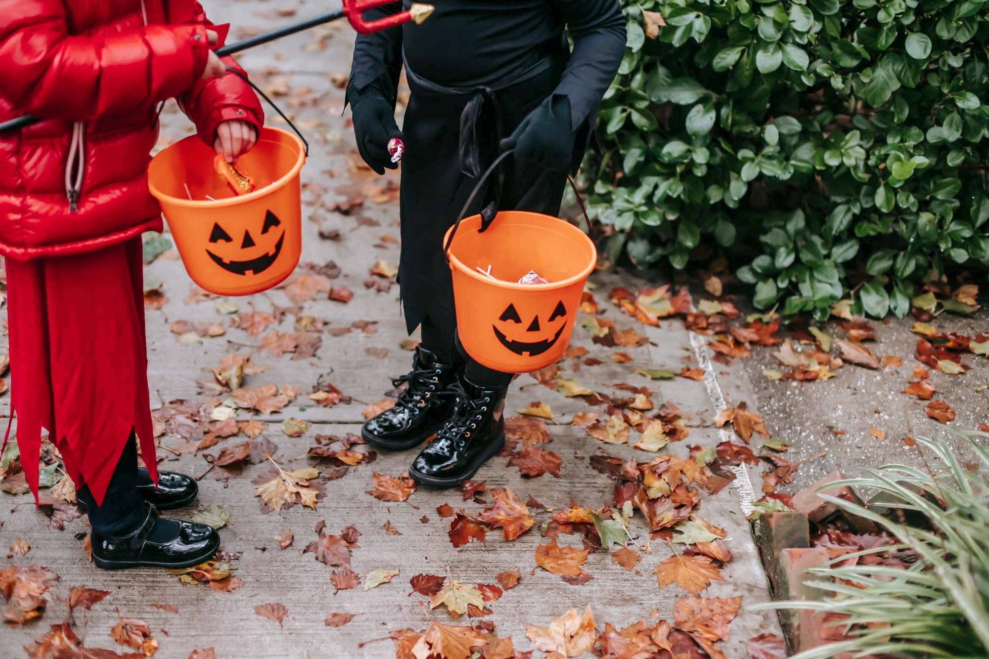 Children holding a Halloween bucket with candy surrounded by autumn leaves.