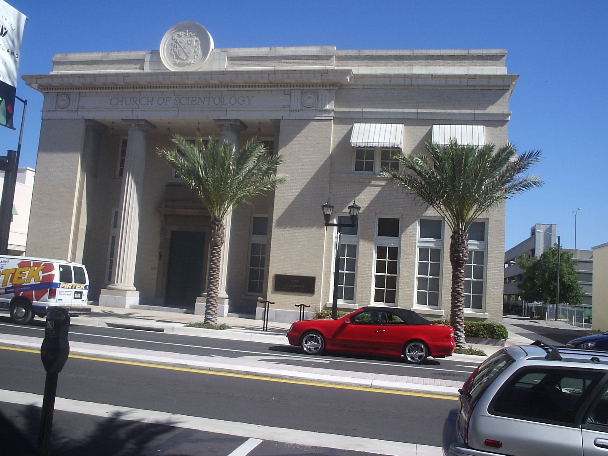Neoclassical stone building with columns and Church of Scientology sign, flanked by palm trees.