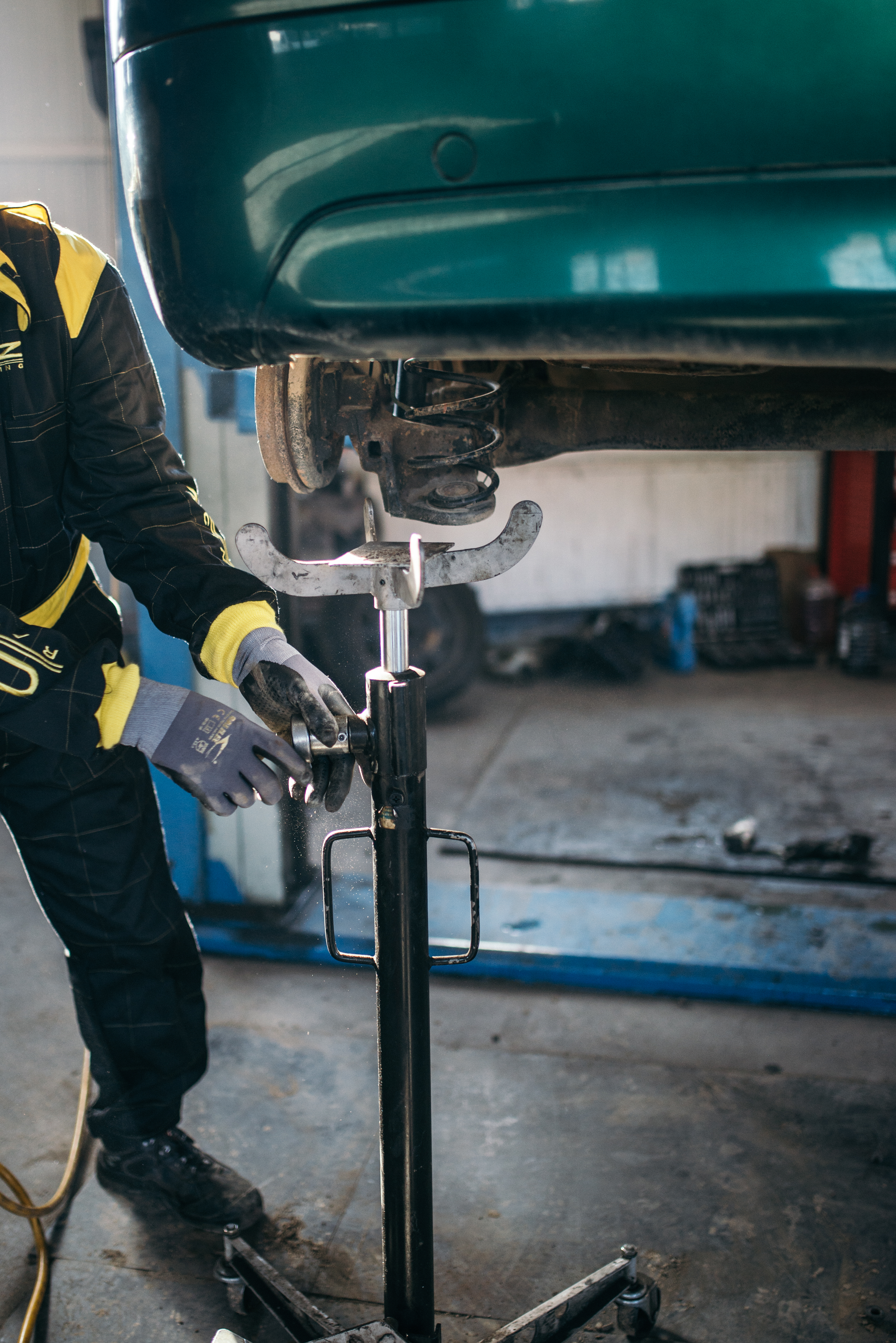 Mechanic in work uniform repairing suspension of a lifted green vehicle in a garage.