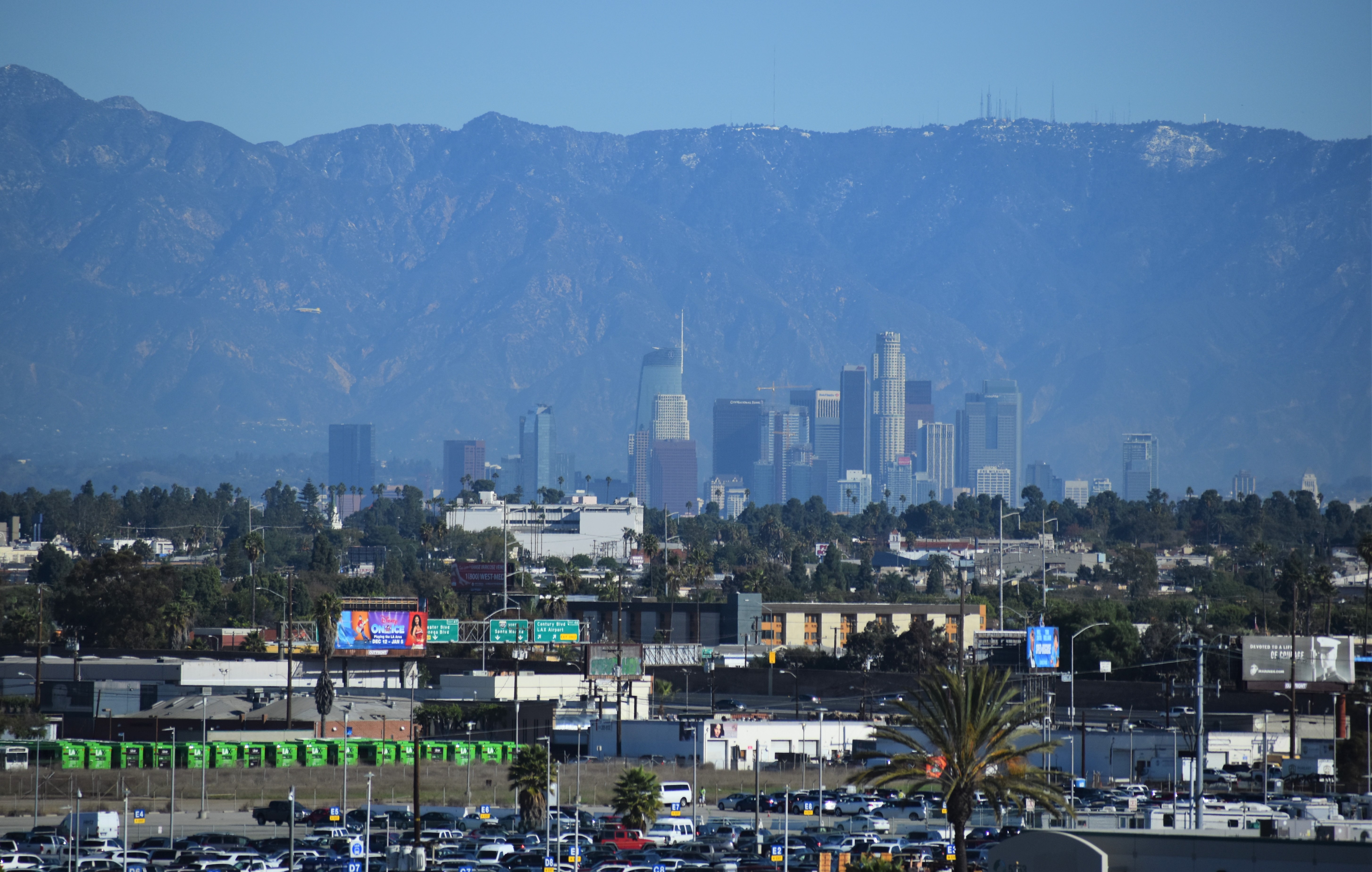 Los Angeles skyline viewed from El Segundo, with a freeway interchange and palm trees in the foreground.