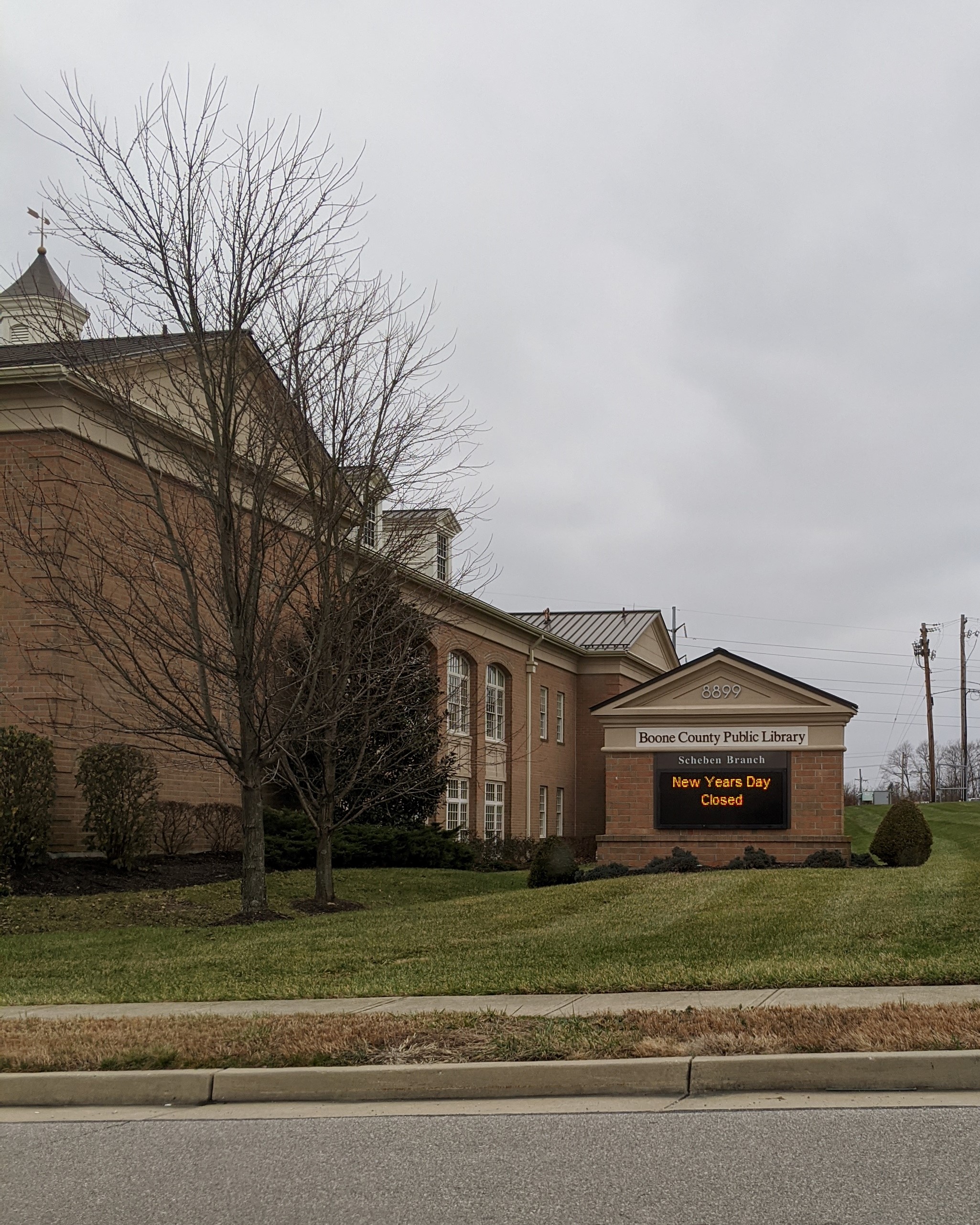 Brick library building exterior with an electronic marquee sign and bare trees.