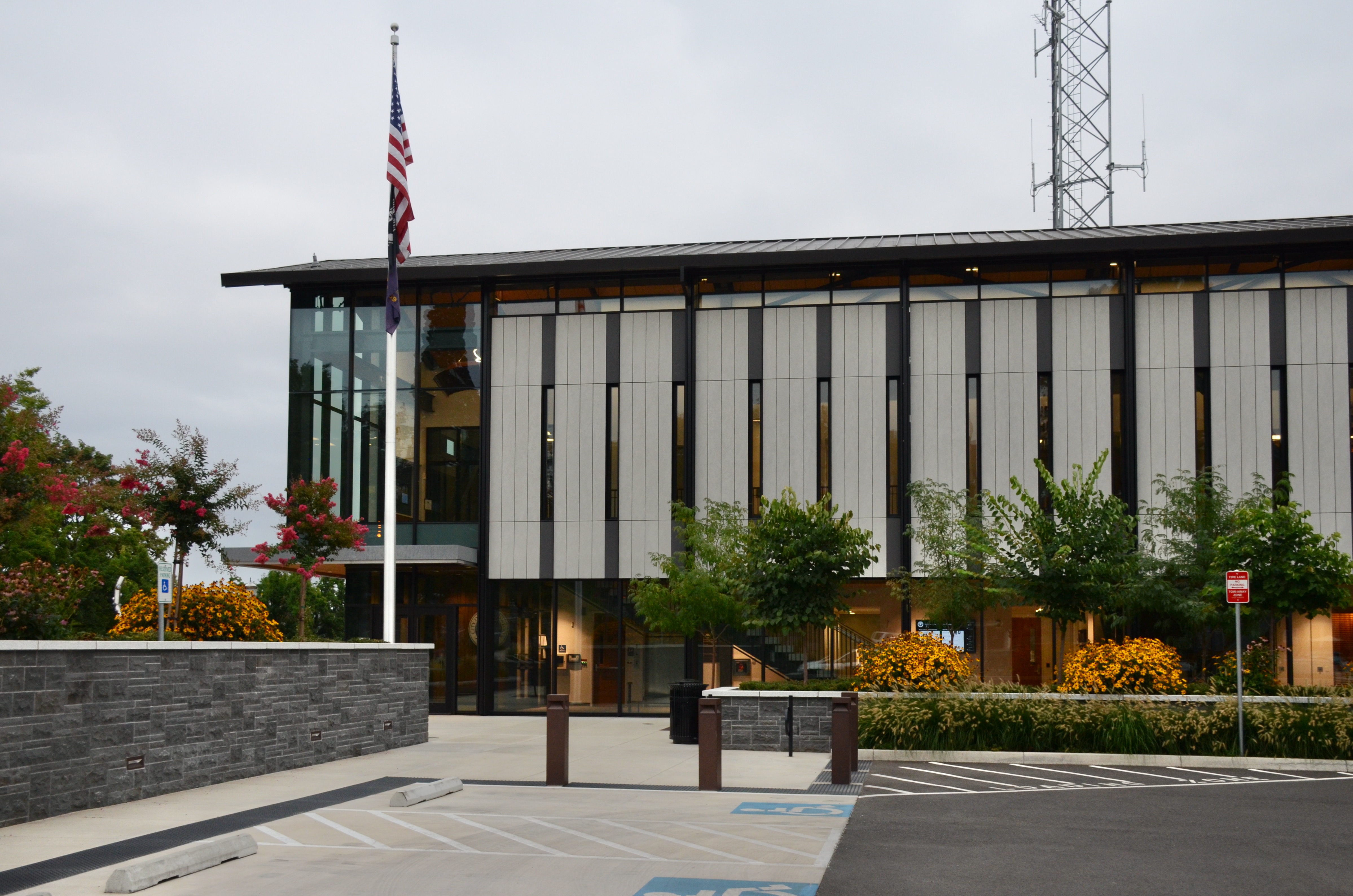 Modern two-story municipal building with glass facade and American flag on a flagpole.