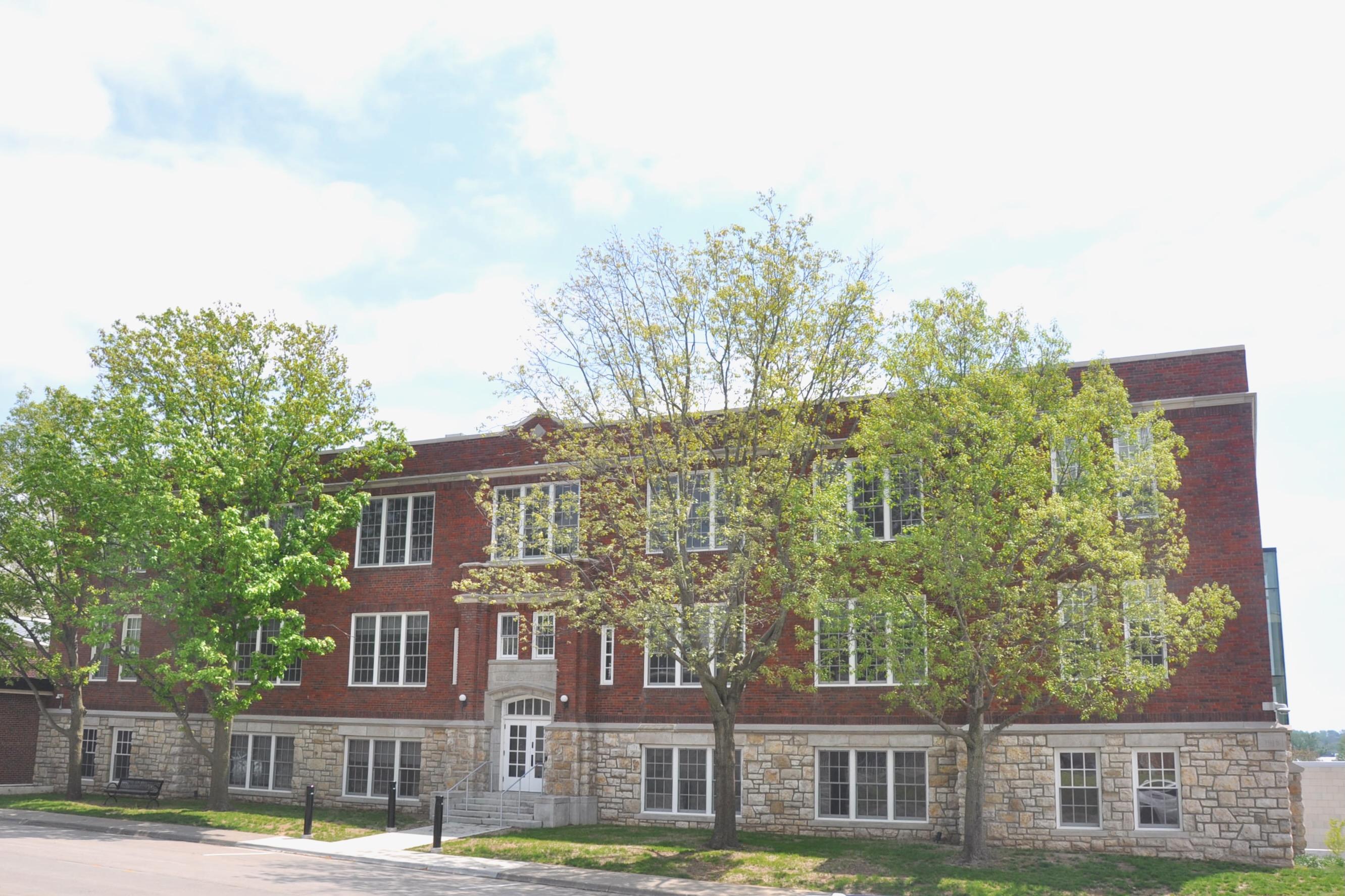 Three-story red brick school building with rows of windows and leafy trees.