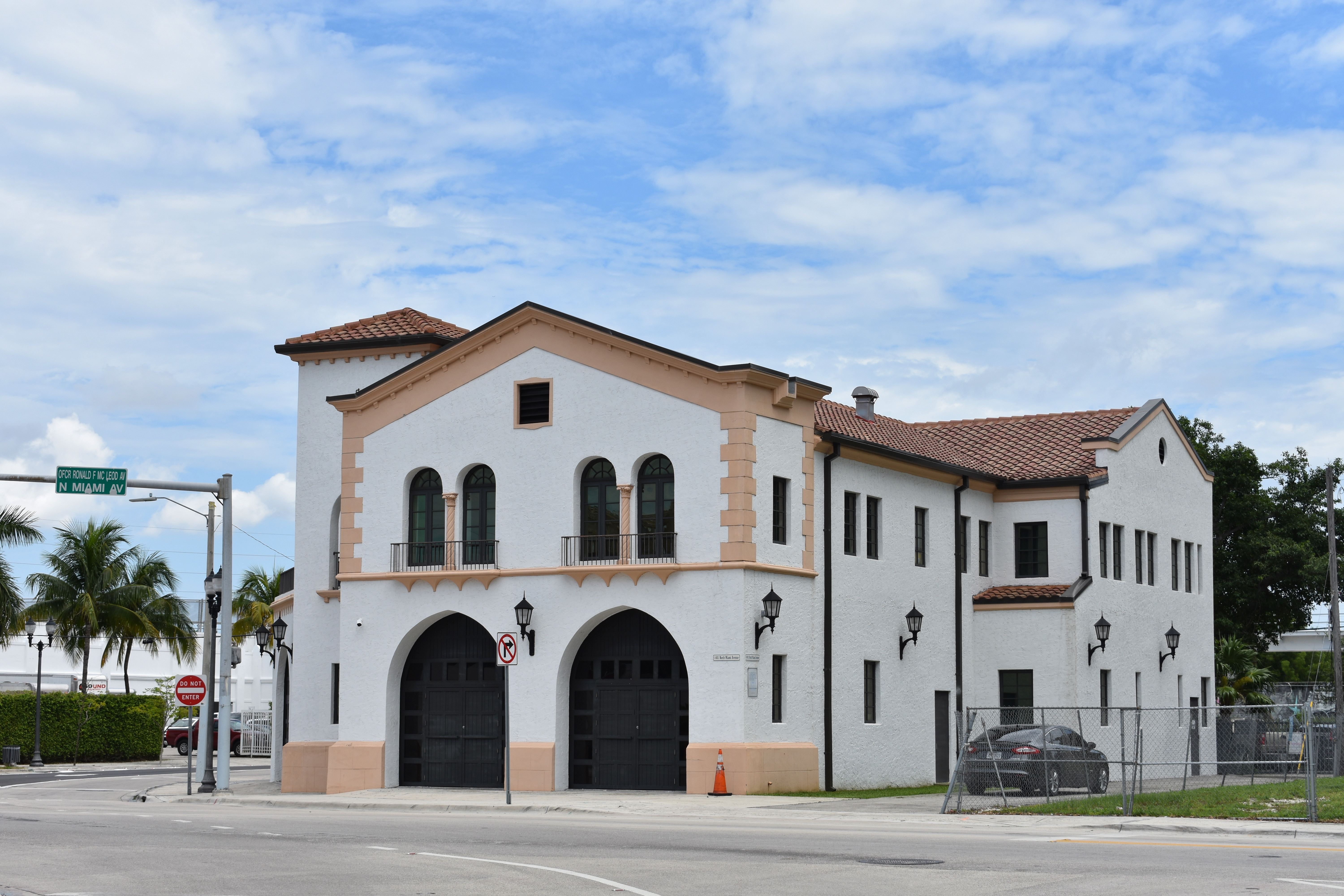 Two-story white stucco fire station on a corner with arched bays and palm trees.
