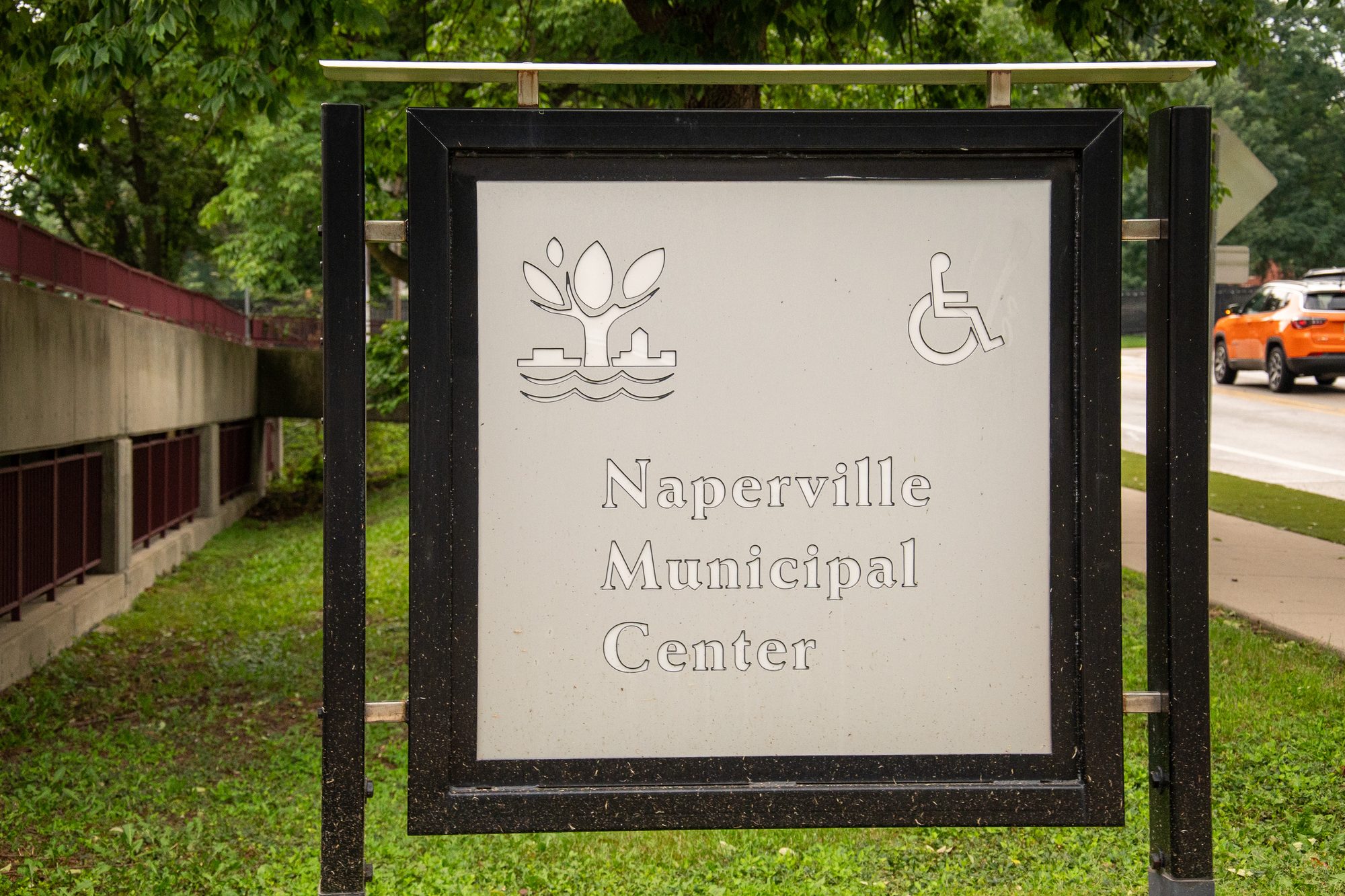 Outdoor monument sign reading Naperville Municipal Center with accessibility symbol and city logo.