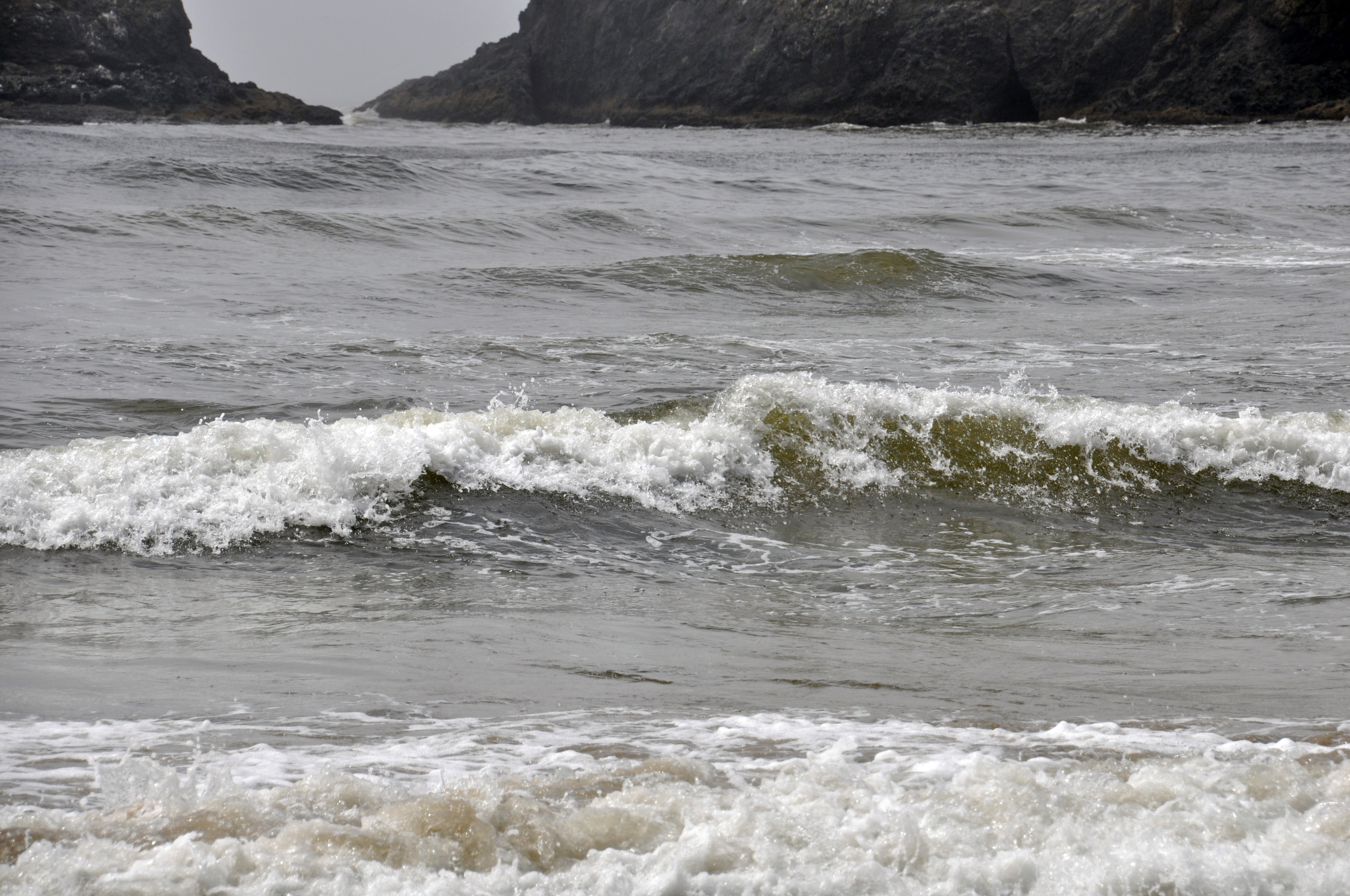 Ocean waves breaking near a rocky shoreline under overcast skies with white foam.