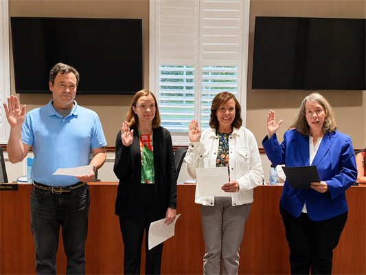 Four adults raise their right hands in an oath-taking ceremony in a formal meeting room.
