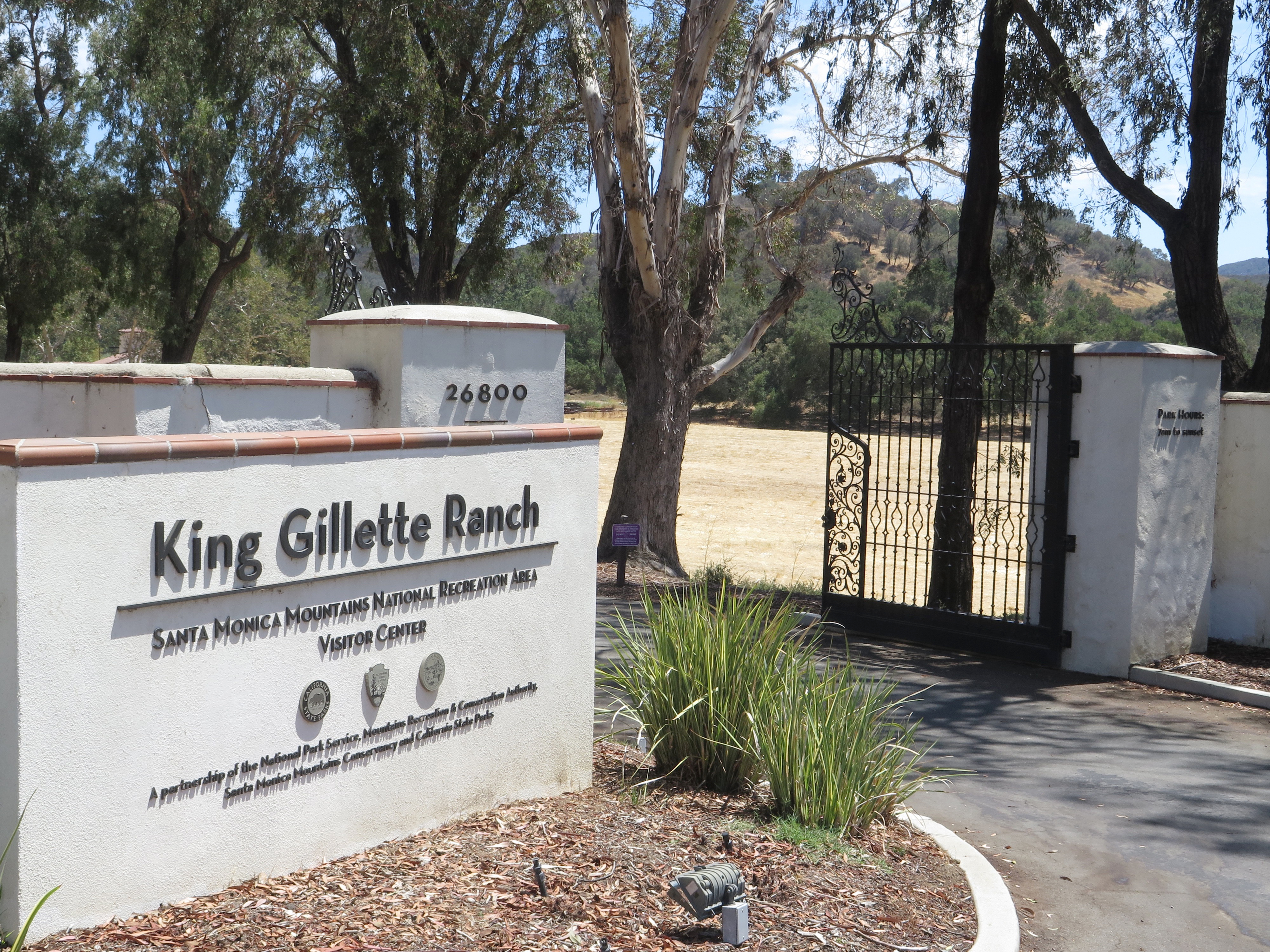 Entrance sign reading 'King Gillette Ranch' beside a wrought-iron gate and eucalyptus trees.