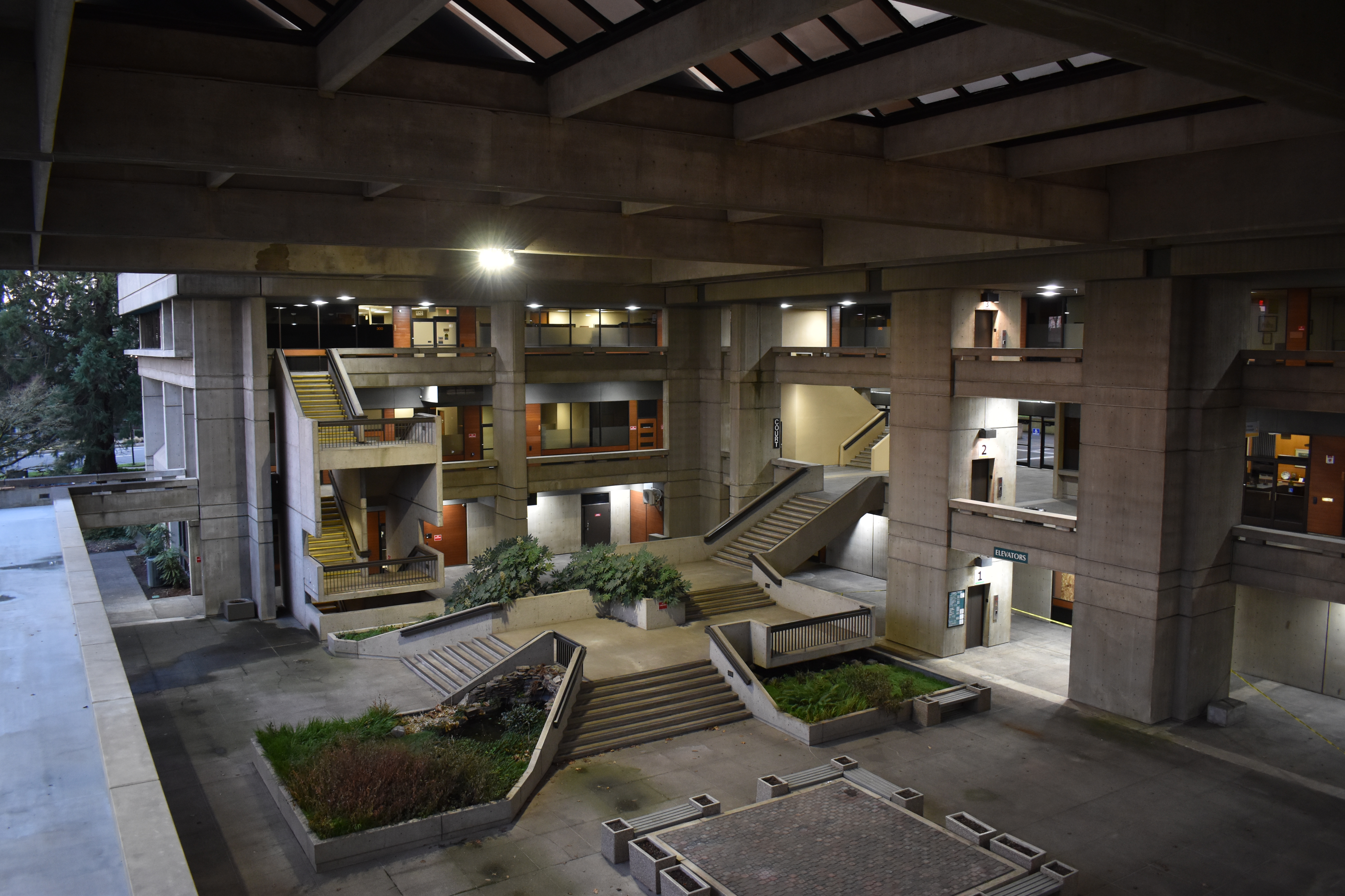 Covered concrete courtyard with multi-level staircases inside a civic building at dusk.