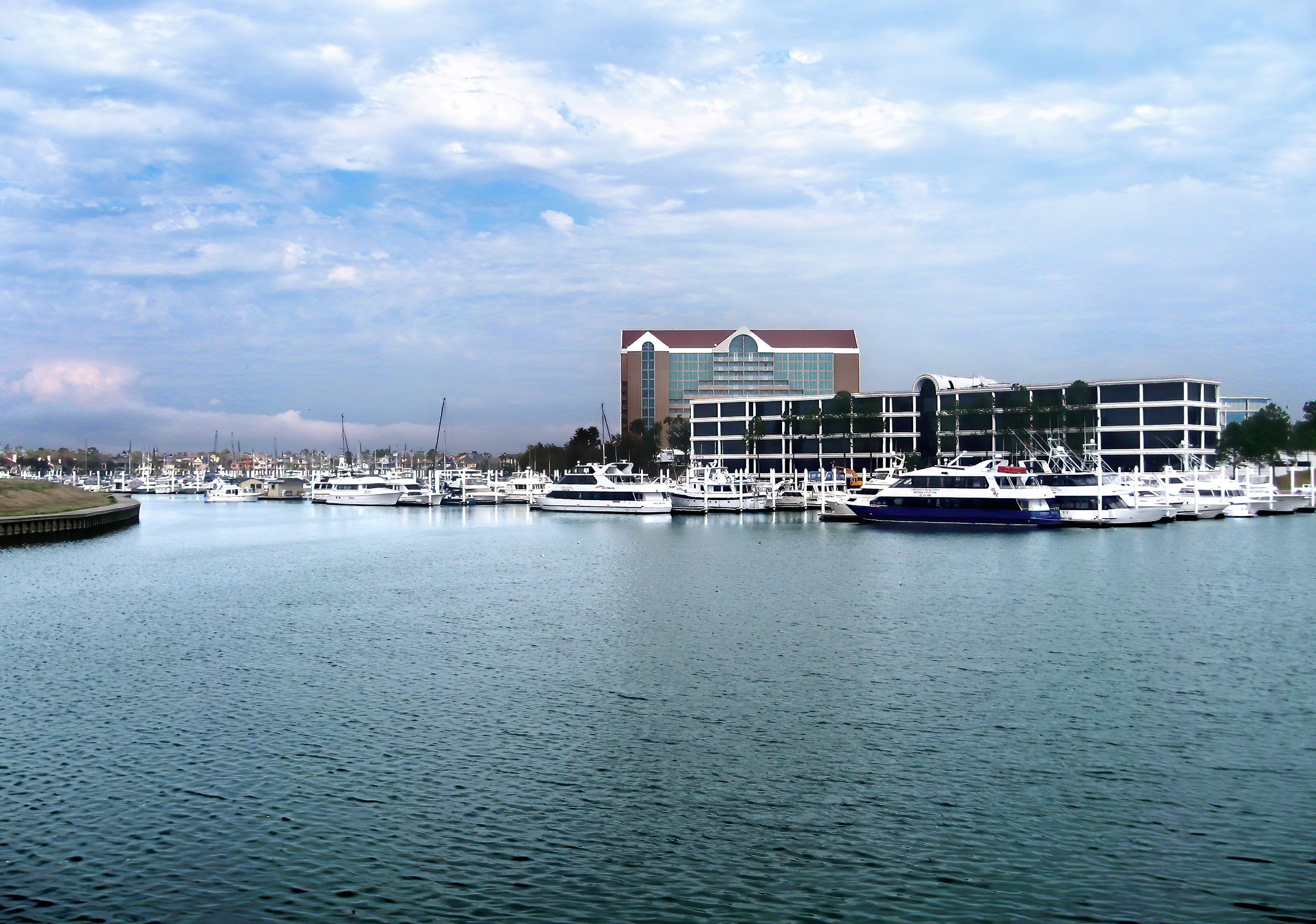 Marina with docked boats in front of a multi-story resort building under a partly cloudy sky.
