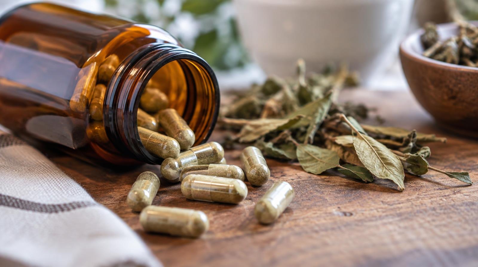 Amber supplement bottle tipped over with capsules and dried leaves on wood surface.