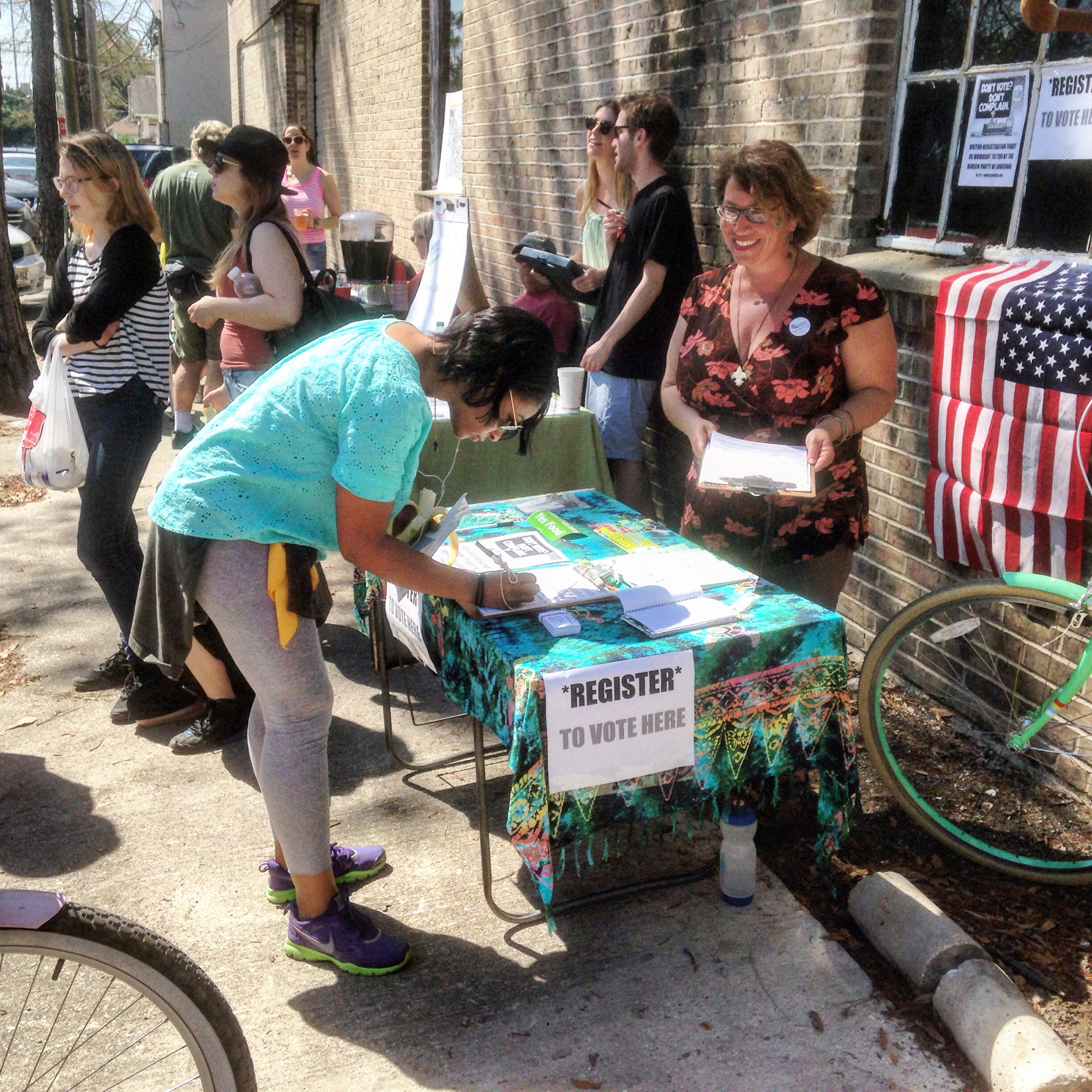 Person filling out forms at a voter registration table with a sign and American flag.