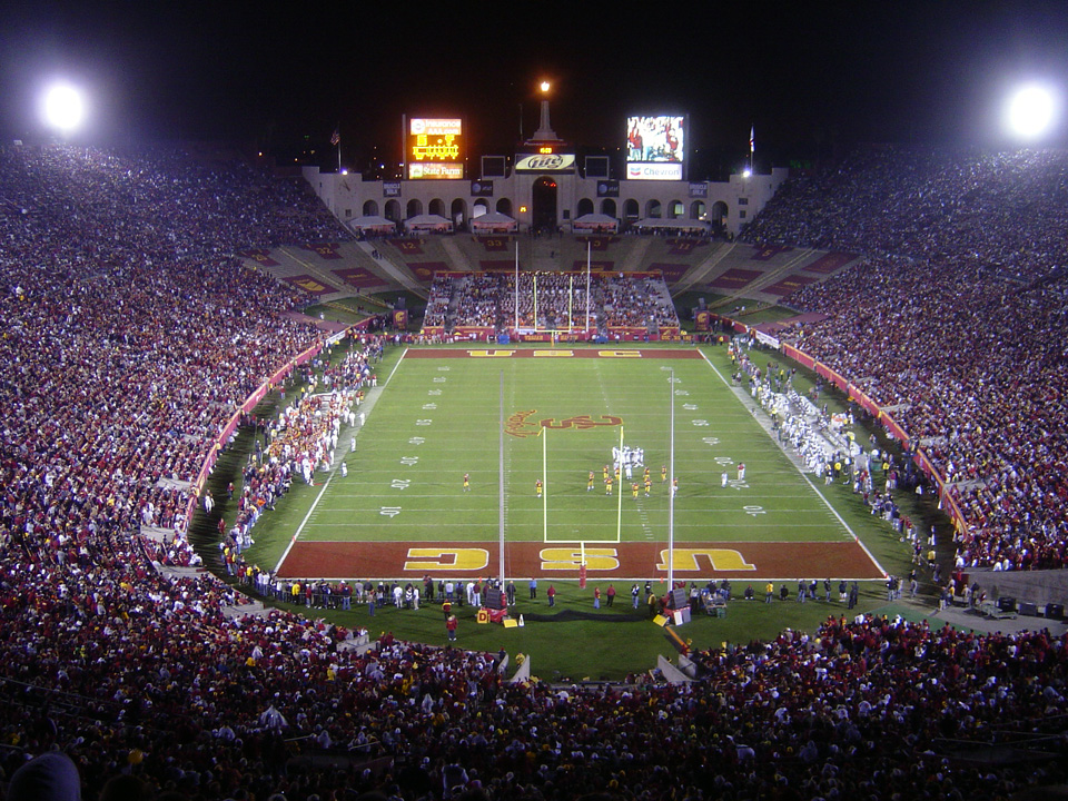 Aerial night view of the Los Angeles Memorial Coliseum filled with spectators during a football game.