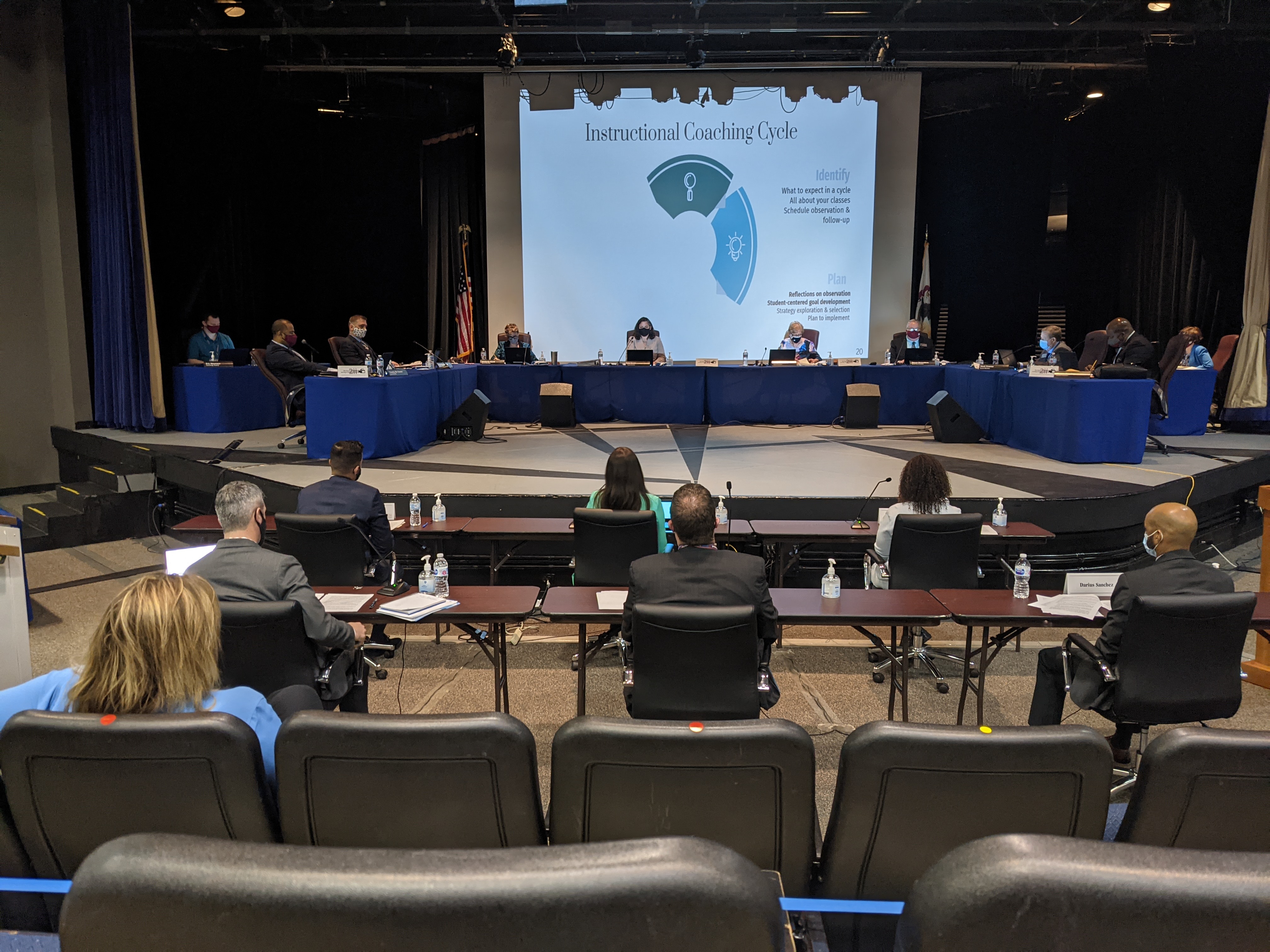 School board members seated at a long curved table on an auditorium stage.