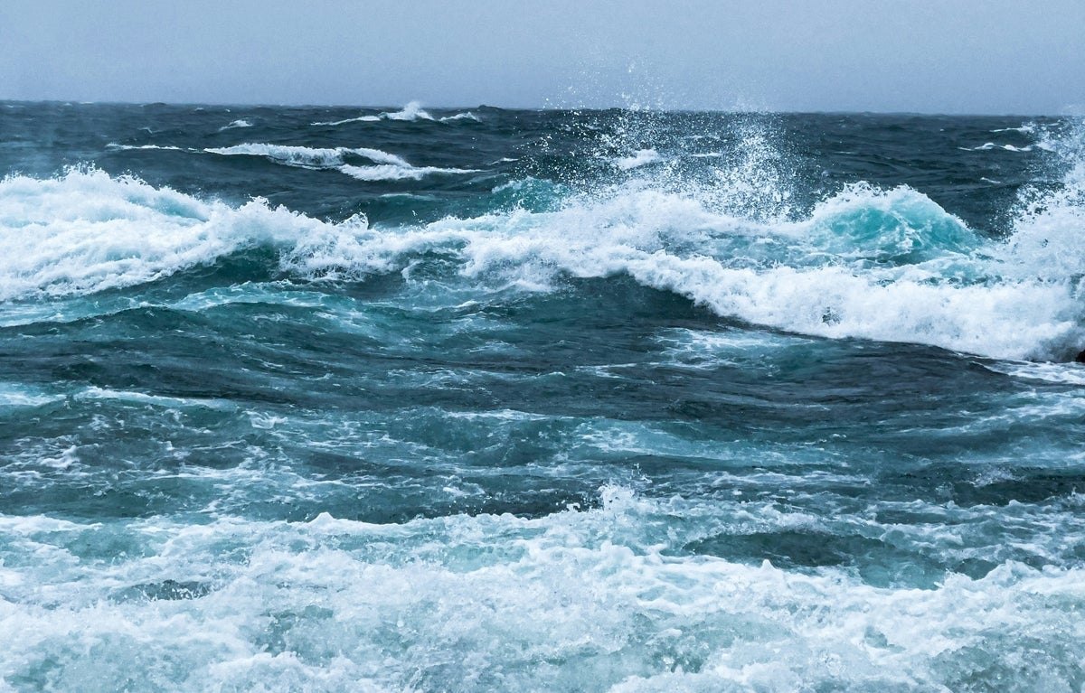 Rough ocean waves with white foam and spray under an overcast grey sky.
