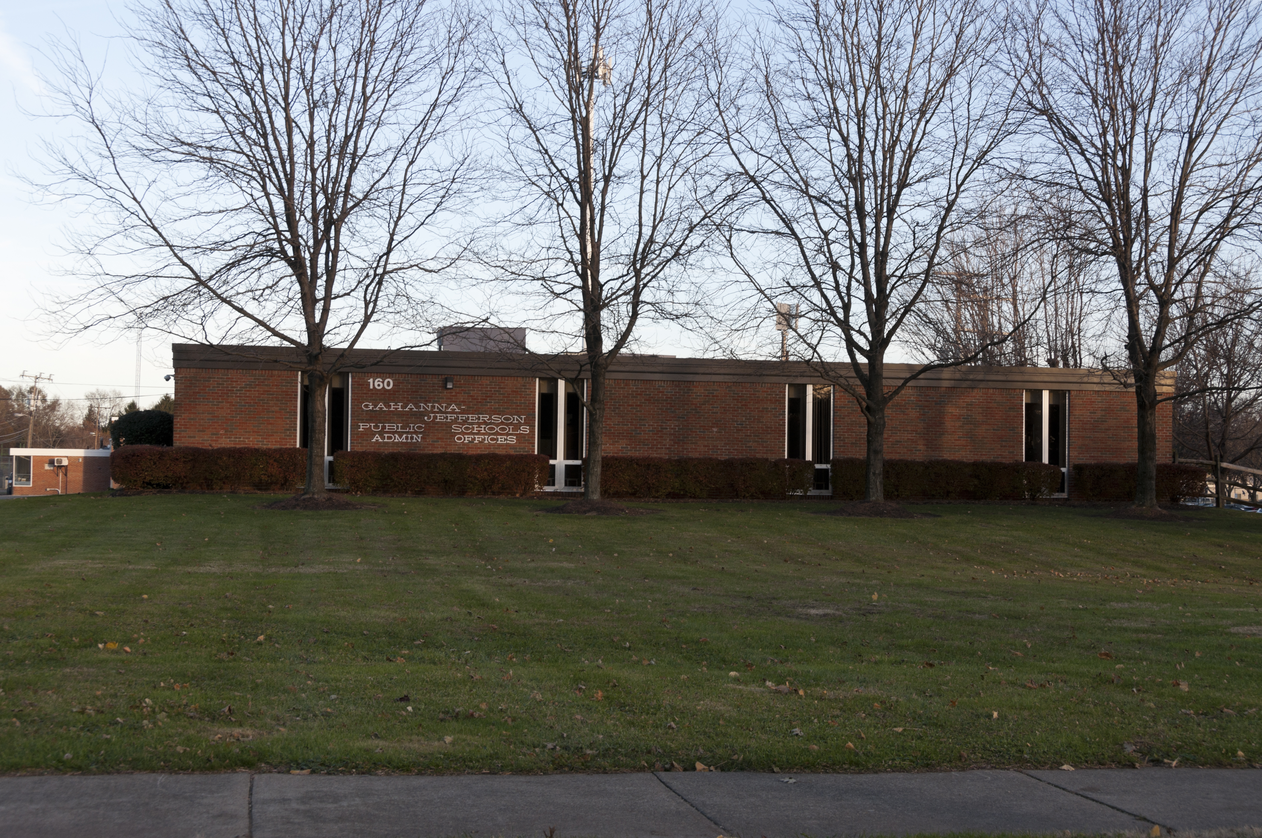 Single-story brick school district administration building with bare trees in front.