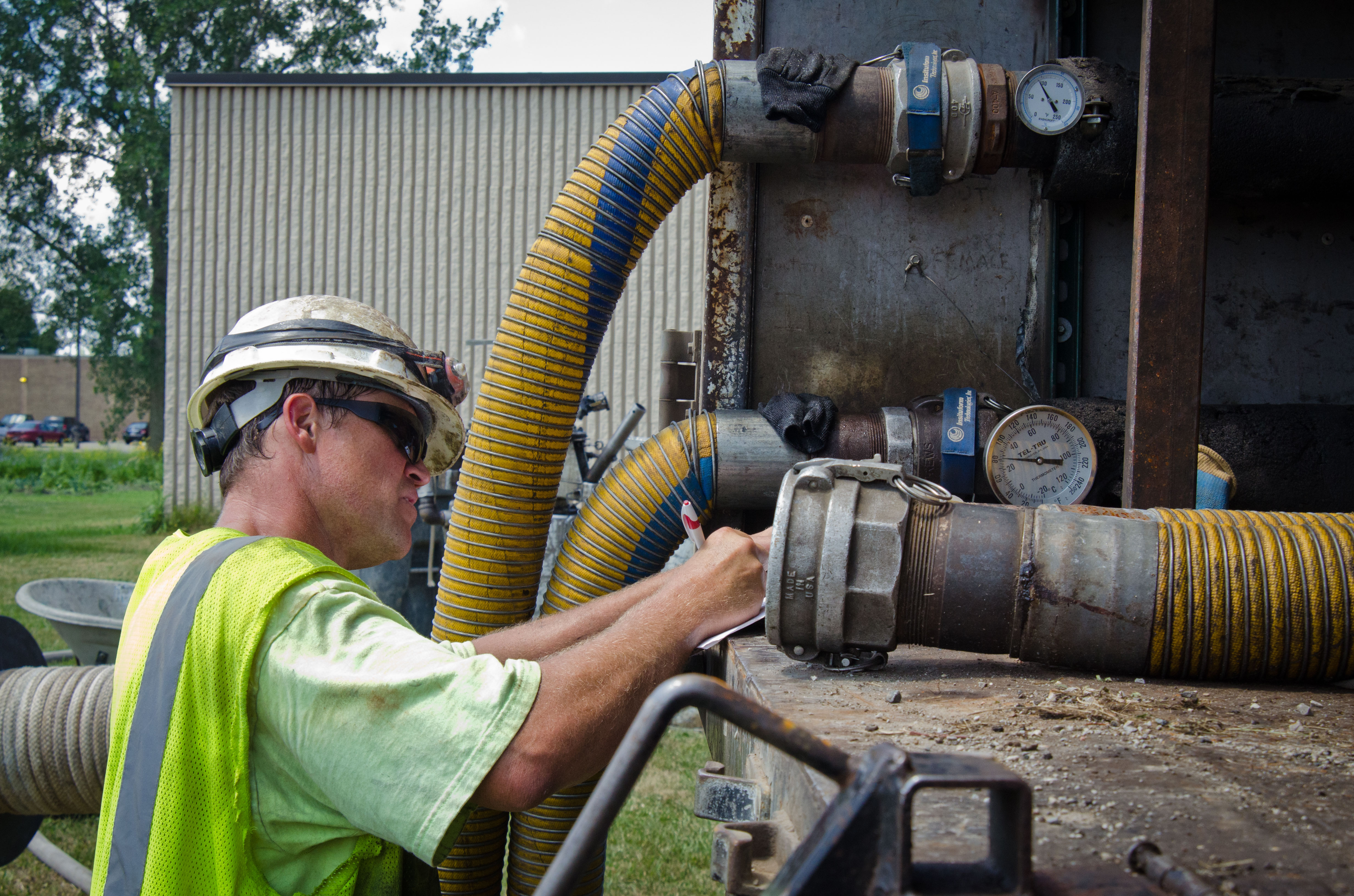 Utility worker in safety vest examining pressure gauges on water infrastructure equipment outdoors.
