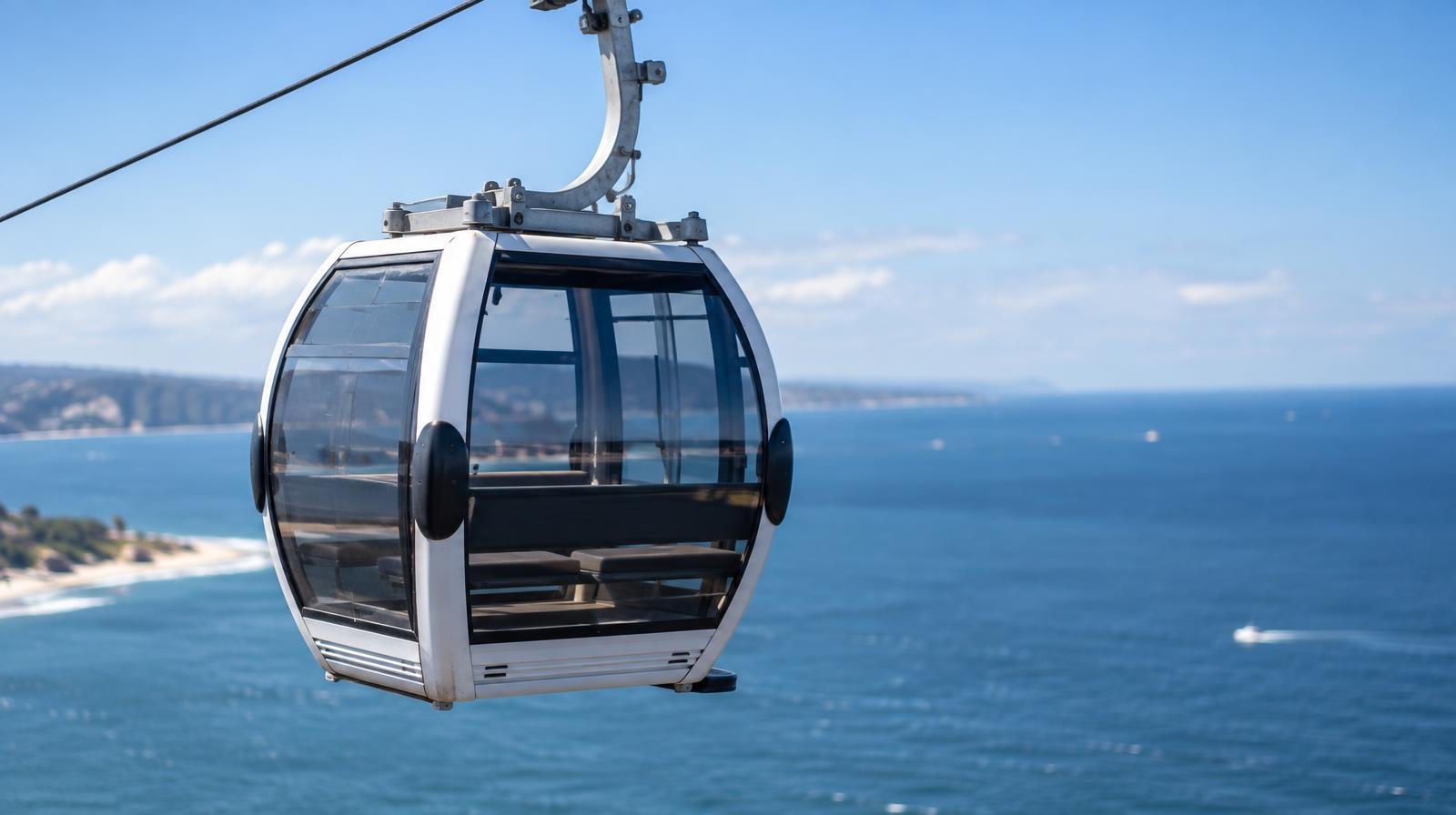 Modern cable car gondola cabin suspended on a wire above open water.