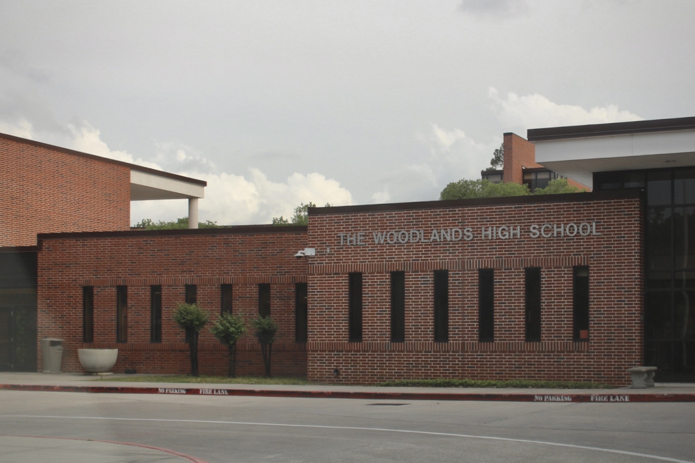 Red brick exterior of The Woodlands High School with school sign in front.