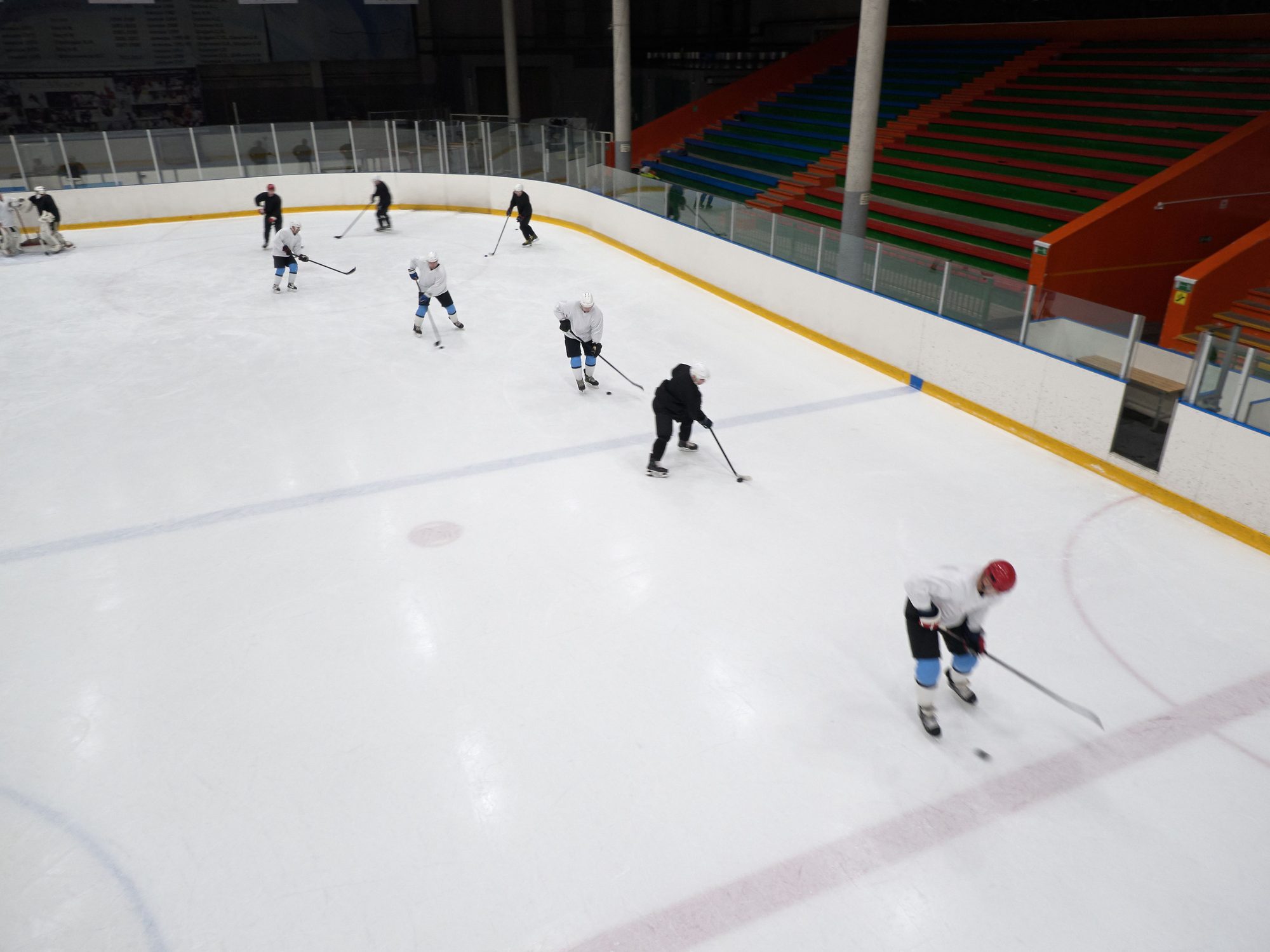 A group of ice hockey players practicing on an indoor rink with vibrant seating area.