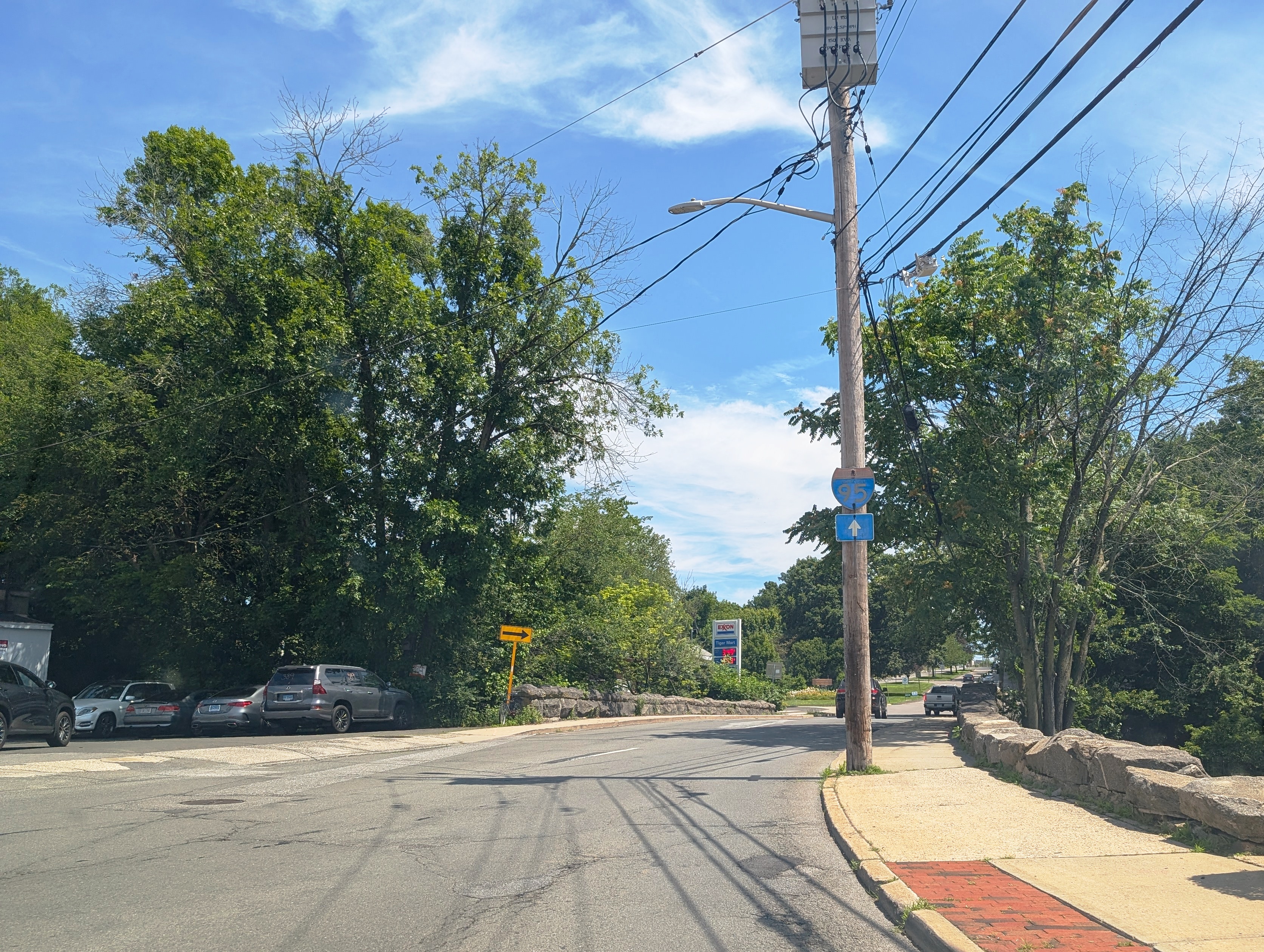Two-lane road with utility poles and overhead wires approaching a traffic circle near the Connecticut border.