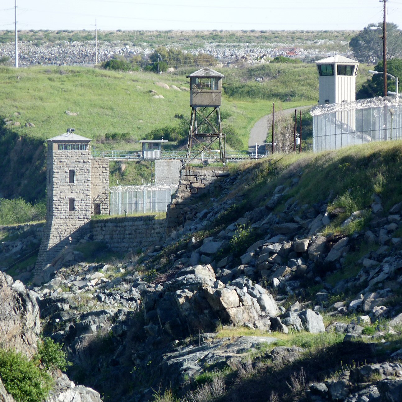 Stone prison wall with guard towers and razor-wire chain-link fencing.