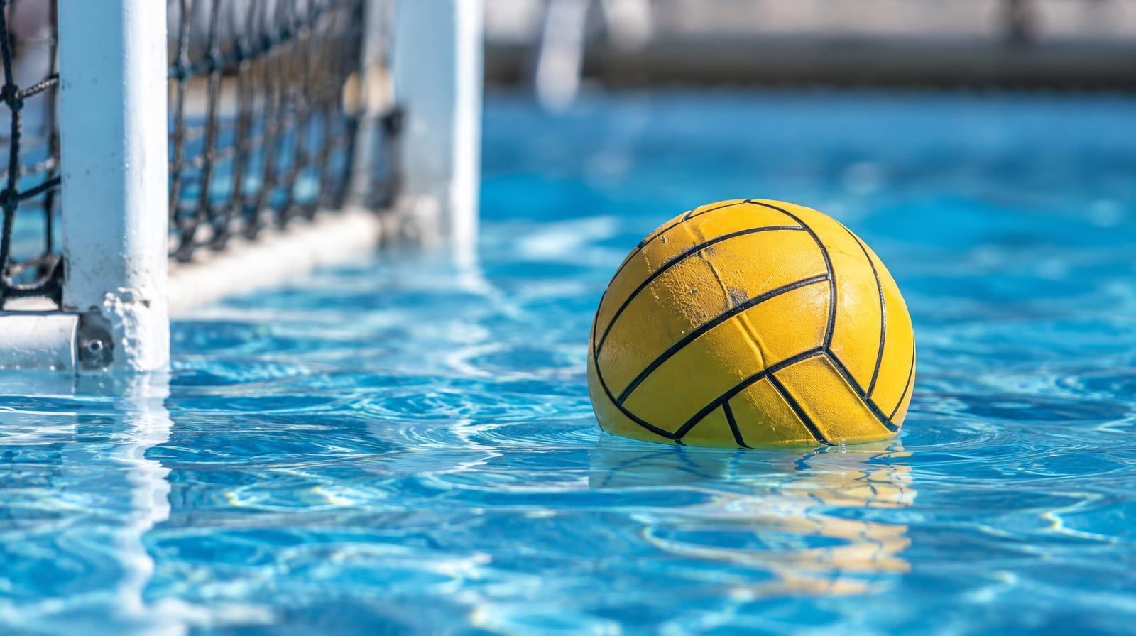 A water polo ball floating on the surface of a bright blue pool near a goal net.