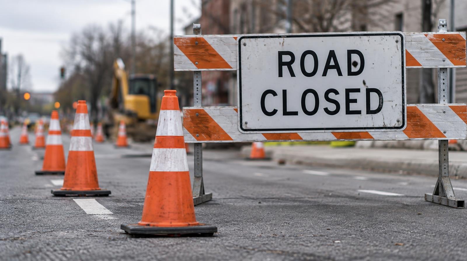 Row of orange traffic cones and a striped barricade blocking a lane of asphalt road.
