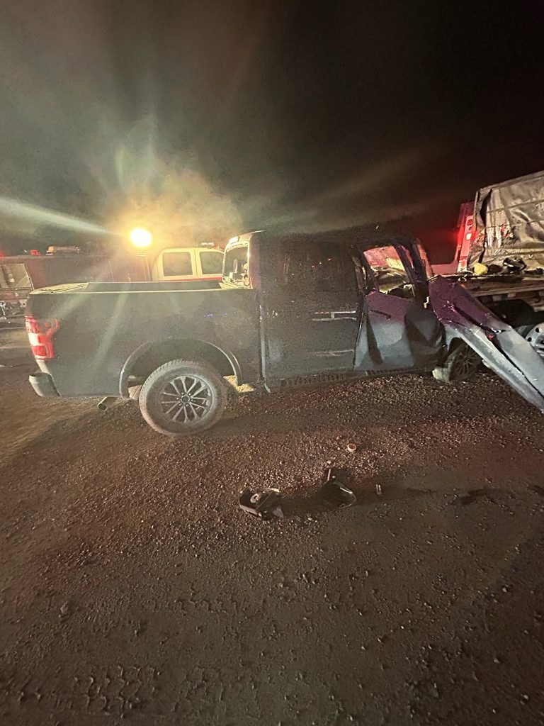 Heavily damaged pickup truck at a nighttime crash scene with emergency lights in background.