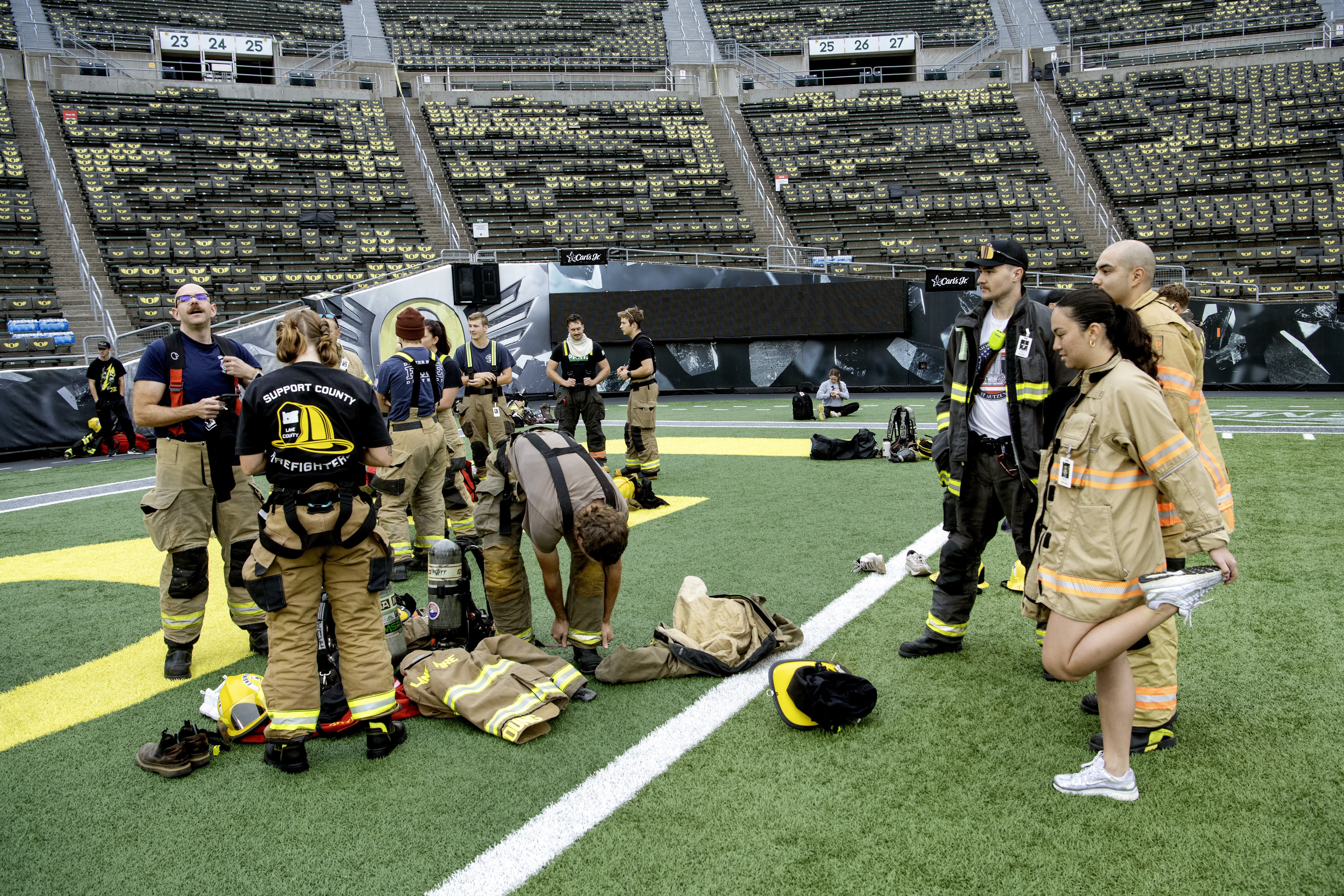 Firefighters in turnout gear stand together on a stadium field after a stair climb.
