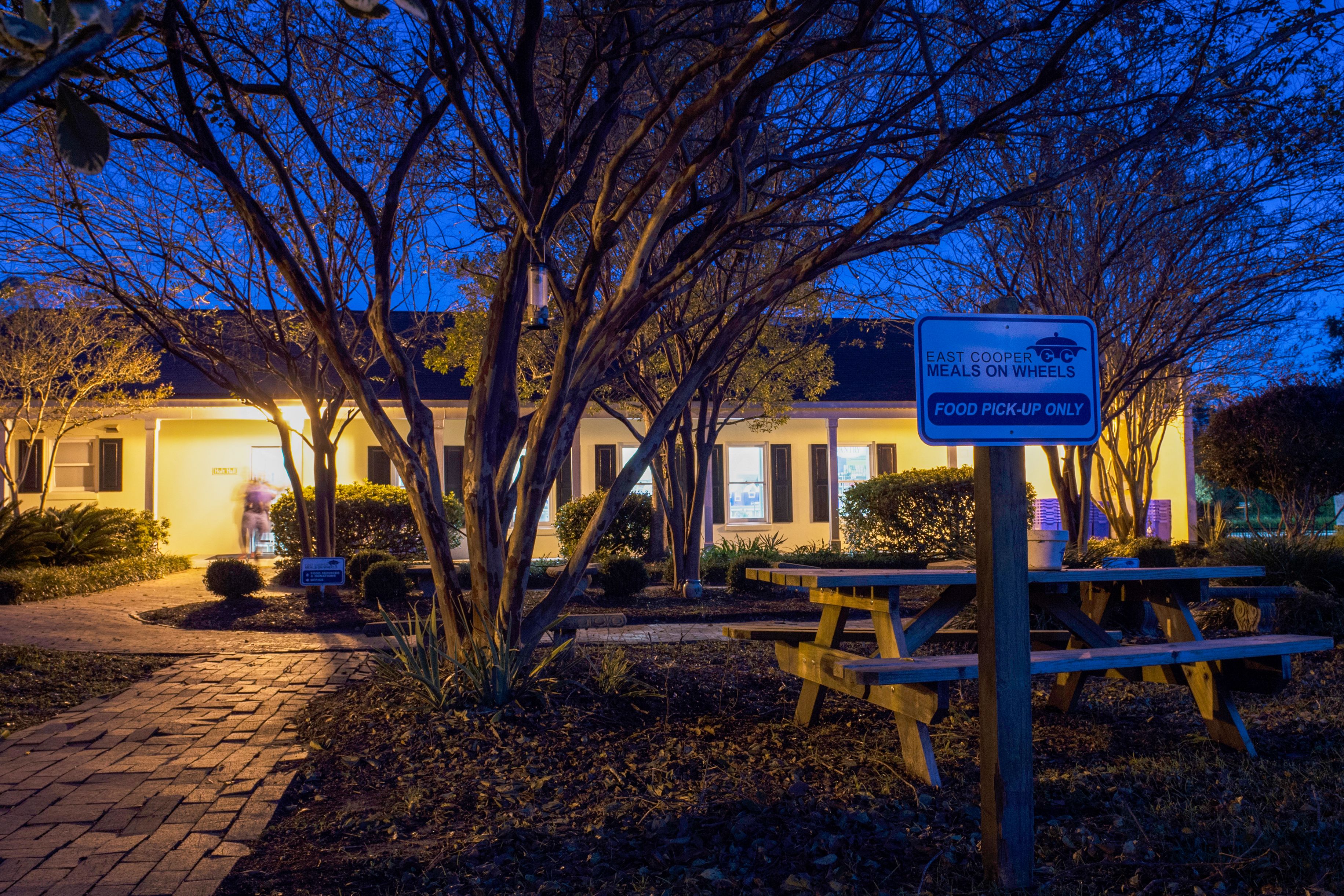 Blue Meals on Wheels sign in front of a lit building at dusk.