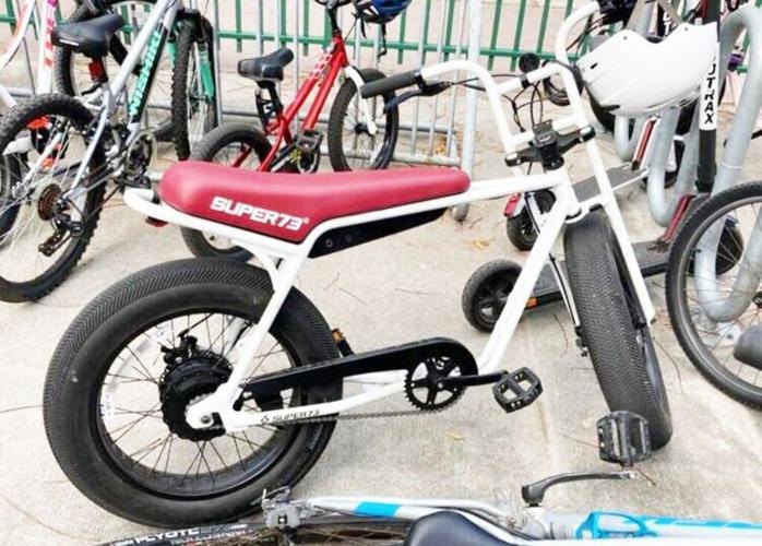 A white Super73 electric bike with a red seat parked in a bike rack among other bicycles.